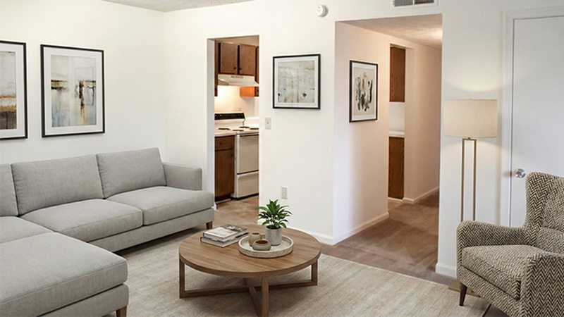 Charming living room with modern gray sofa, wooden coffee table, and elegant wall art, connecting to a cozy kitchen and well-lit hallway.