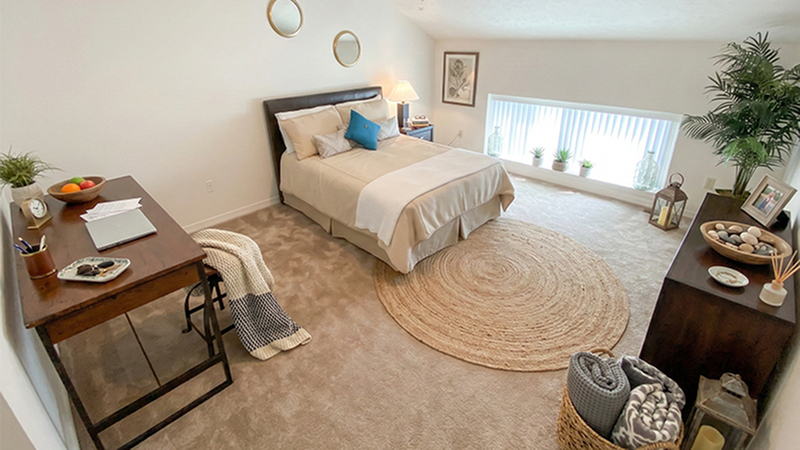 Inviting bedroom with cozy decor, featuring a plush bed, elegant desk, and large window offering natural light in a serene space.