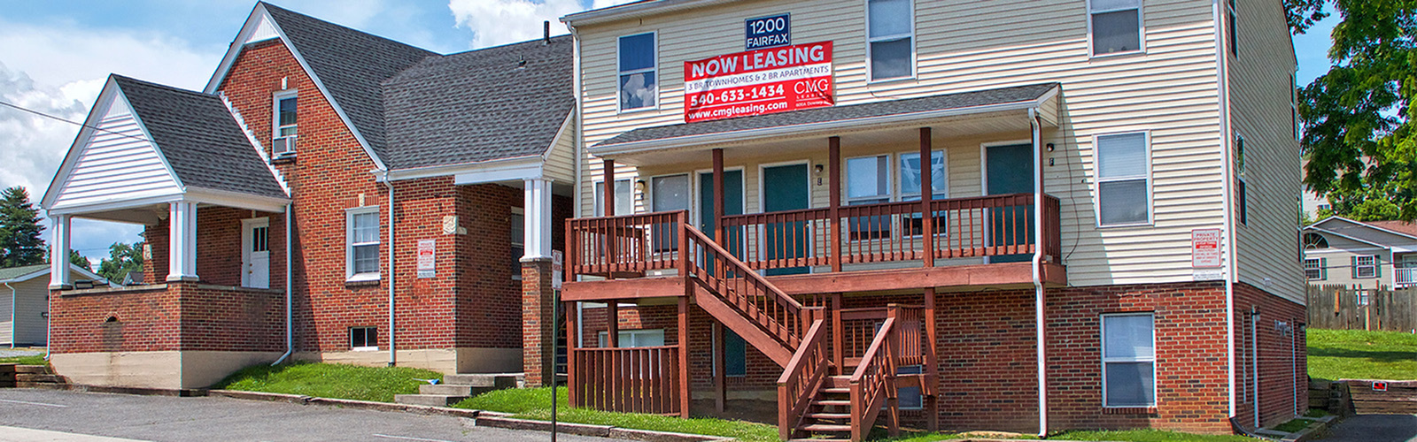 Charming brick apartment building with welcoming front porch and spacious wooden balcony, now leasing 1-2 bedroom homes in a vibrant neighborhood.