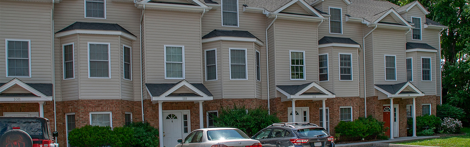 Charming townhouse row with elegant bay windows, a well-maintained facade, and lush greenery, offering modern suburban living.