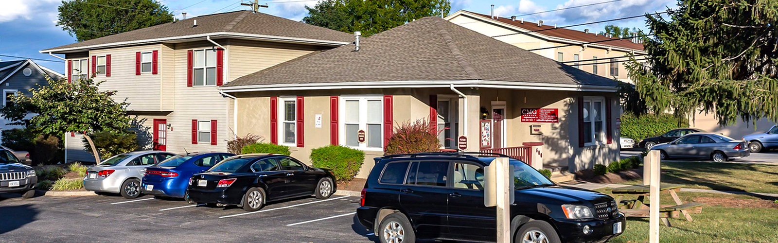 Charming apartment complex with picturesque landscaping, ample parking, and inviting architectural design set under a bright blue sky.