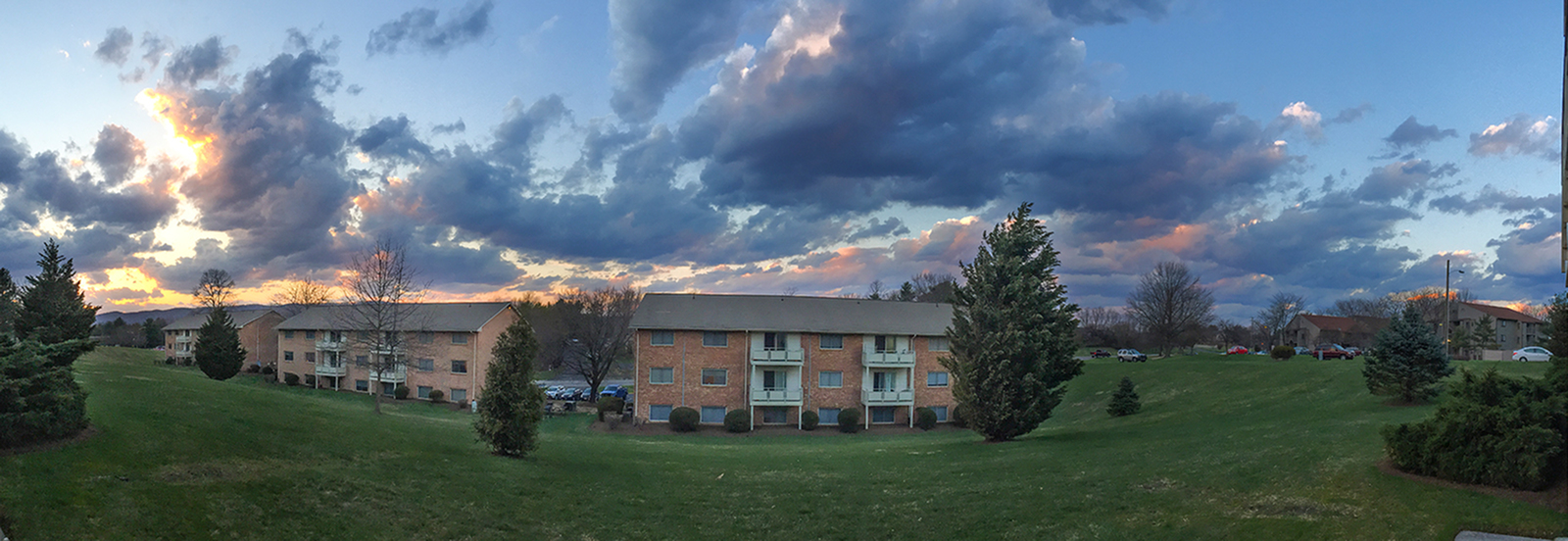 Charming brick apartment complex surrounded by lush greenery under a spectacular, dramatic sunset sky.