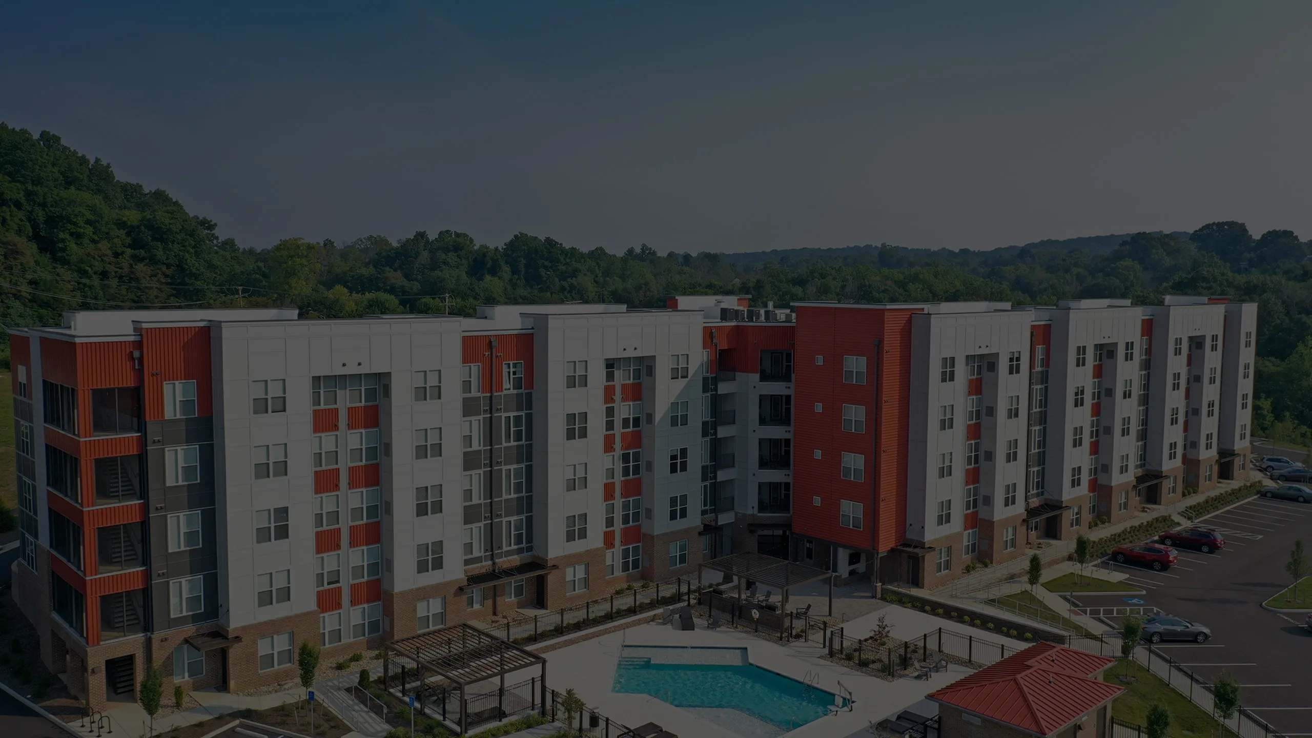 Modern apartment complex with sleek architecture, vibrant red accents, and a central swimming pool surrounded by lush greenery.
