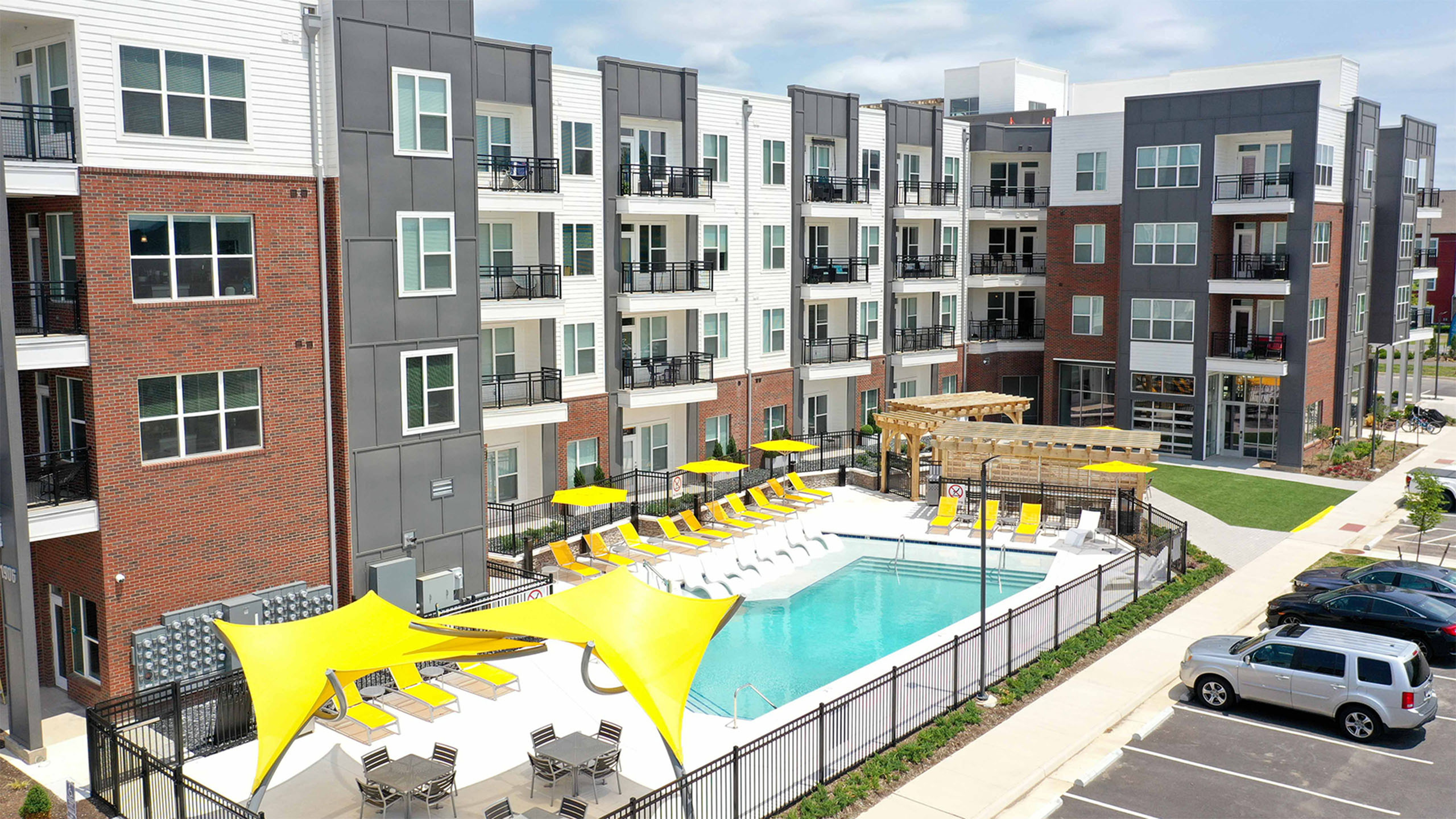 Modern apartment complex showcasing a refreshing outdoor pool with vibrant yellow umbrellas and sleek sun loungers, set against contemporary architecture.
