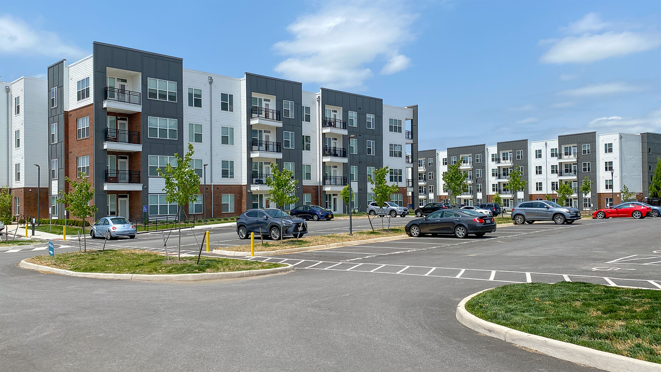 Modern apartment complex featuring sleek, multi-story buildings with private balconies and ample parking space, surrounded by well-maintained greenery.