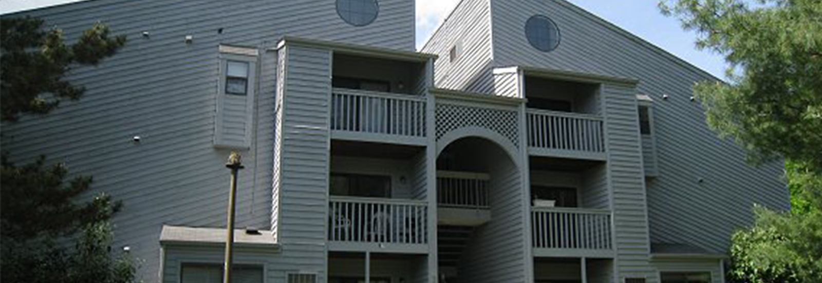 Modern apartment building with distinctive geometric architecture, featuring spacious balconies and surrounded by lush greenery.