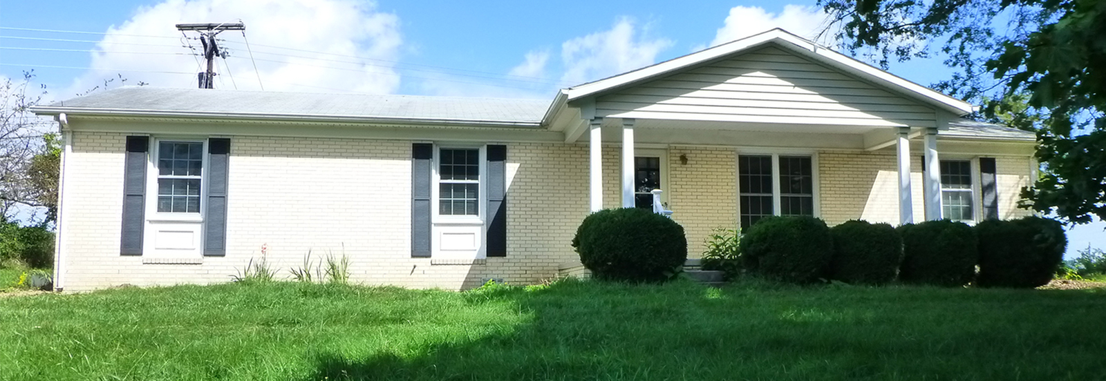 Charming single-story home with classic brick exterior, surrounded by lush greenery and featuring a welcoming front porch.