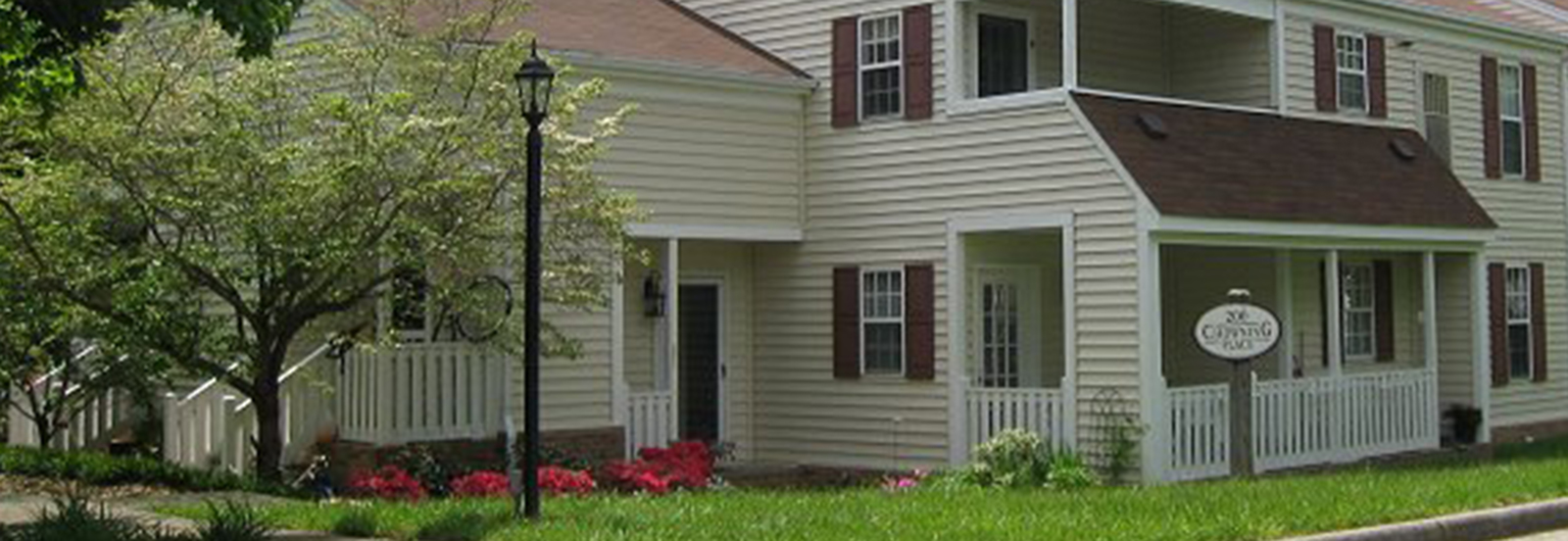 Charming two-story townhouse with classic white siding, inviting front porch, and lush greenery in a peaceful neighborhood.