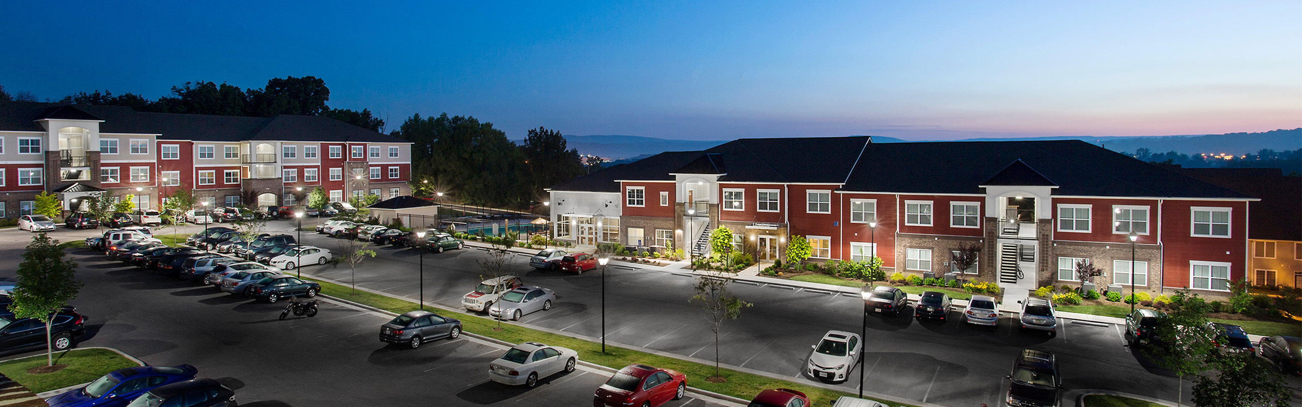 Charming evening view of a modern apartment complex with elegant architecture and ample parking, set against a serene twilight sky.