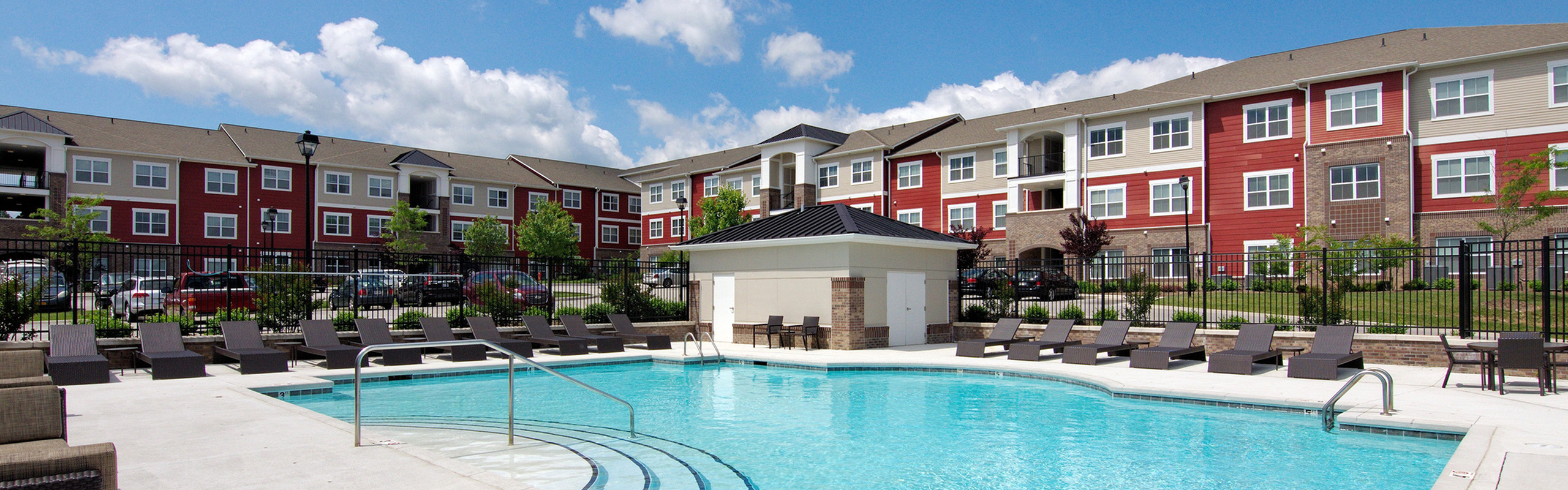 Luxurious apartment complex with an inviting pool, surrounded by stylish sun loungers and scenic landscaping.