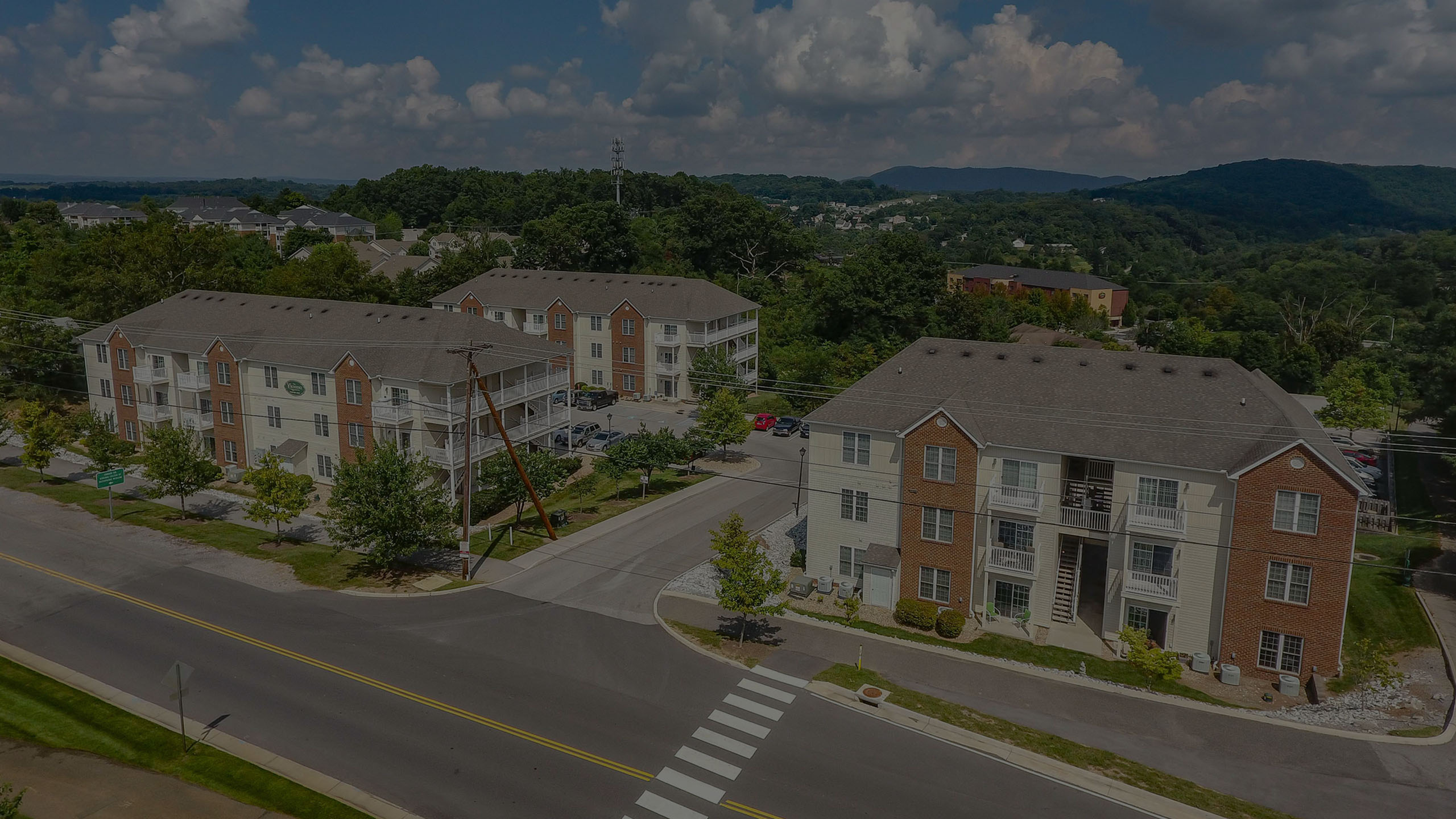 Aerial view of charming apartment buildings surrounded by lush greenery, featuring ample parking and a serene neighborhood setting.