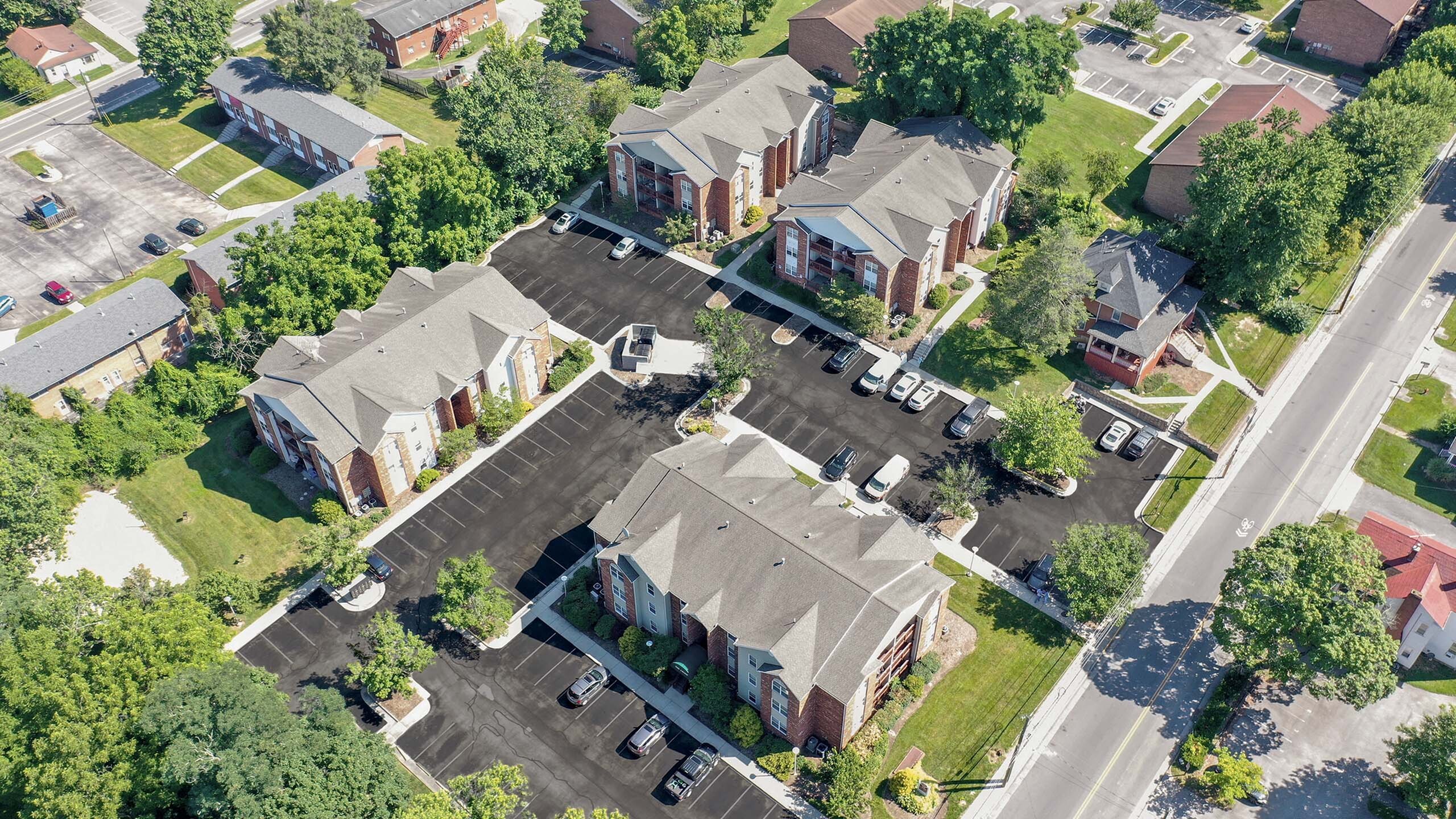 Aerial view of charming apartment complex surrounded by lush greenery and spacious parking, showcasing vibrant community living.