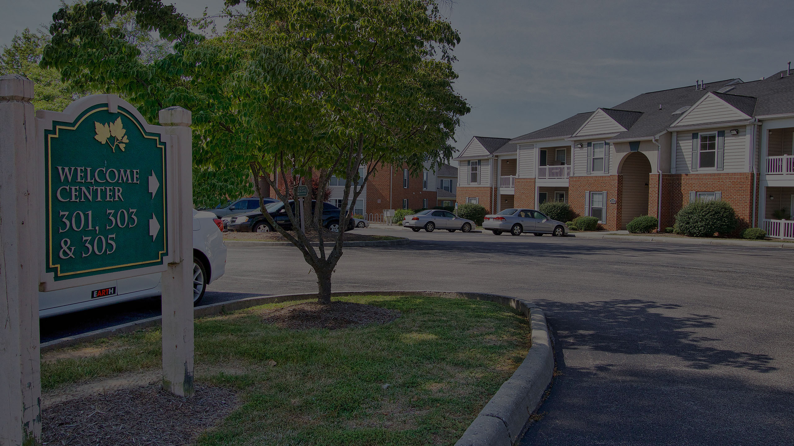 Inviting apartment complex with welcoming fa&ccedil;ade and lush surroundings, featuring a prominent entrance sign directing to the welcome center.