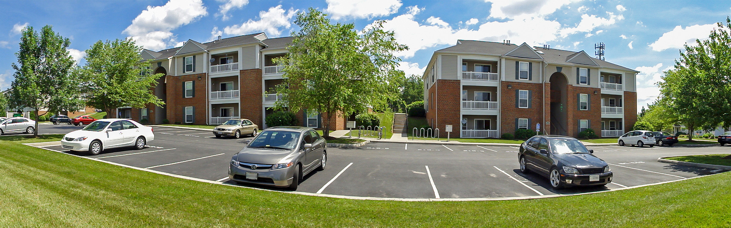 Charming apartment complex with lush greenery, ample parking, and inviting balconies under a bright blue sky.