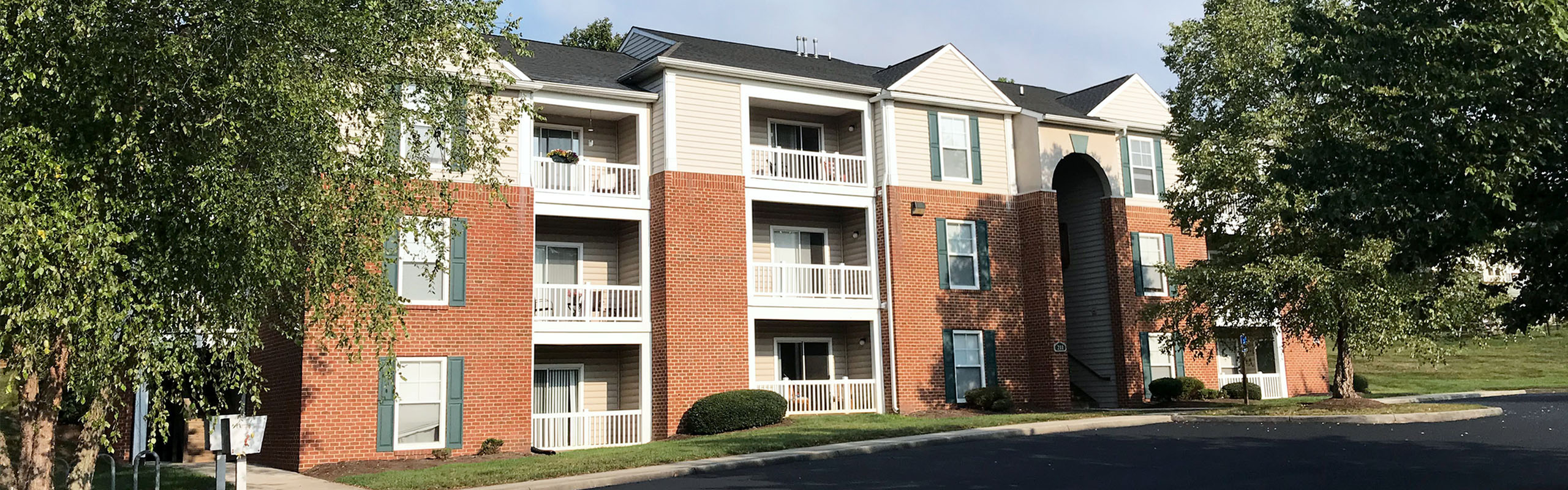 Charming brick apartment building with private balconies, nestled in a lush green landscape.