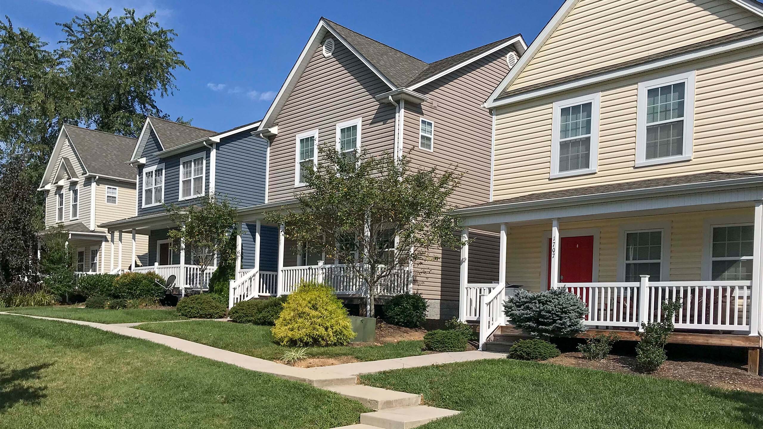 Charming row of modern suburban homes with colorful exteriors and inviting front porches, set against a backdrop of lush greenery.