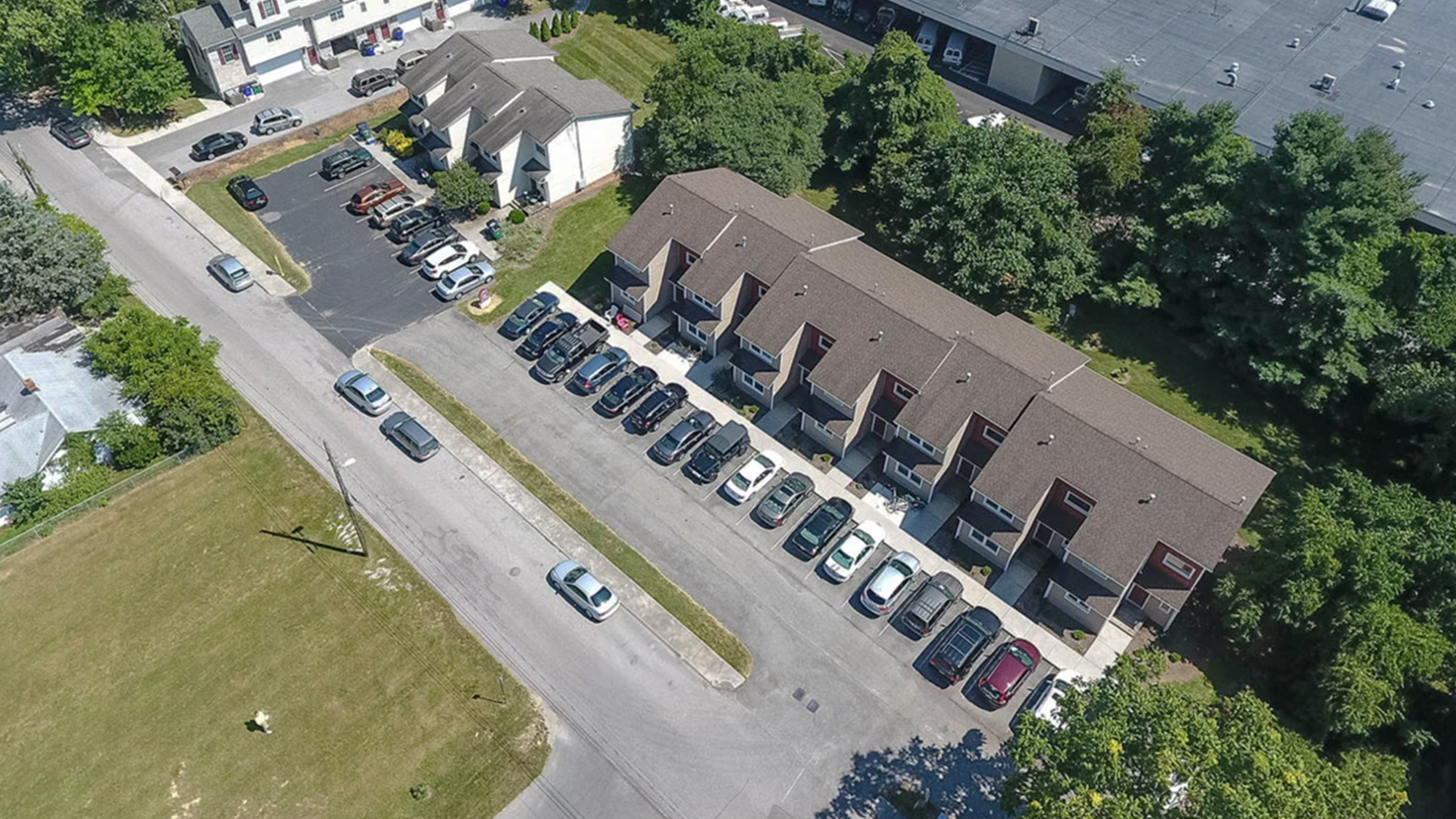 Aerial view of charming townhomes with ample parking and surrounded by lush greenery, offering a peaceful suburban lifestyle.