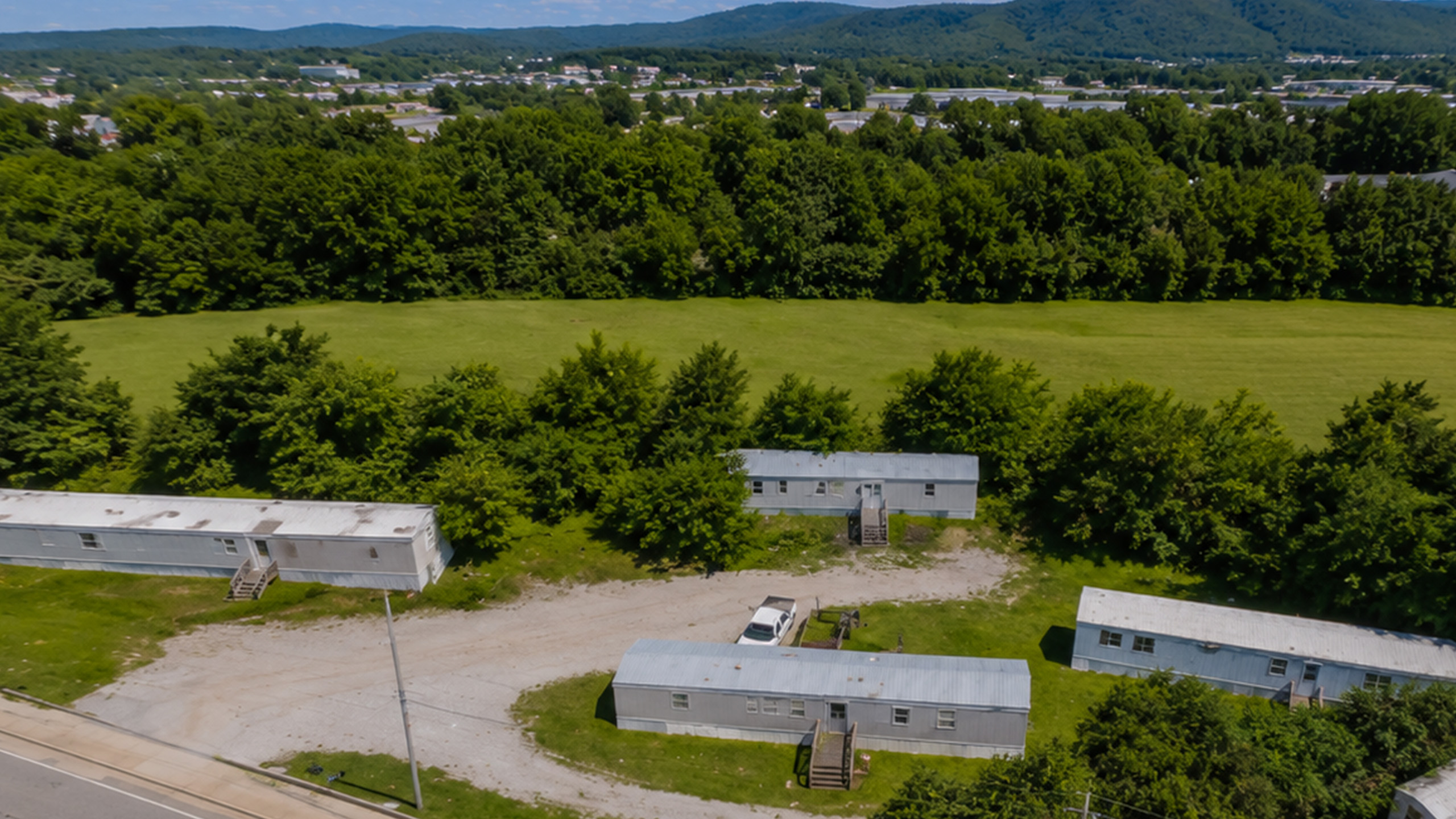 Charming aerial view of cozy mobile homes surrounded by lush greenery and rolling hills, offering tranquil living in nature&rsquo;s embrace.