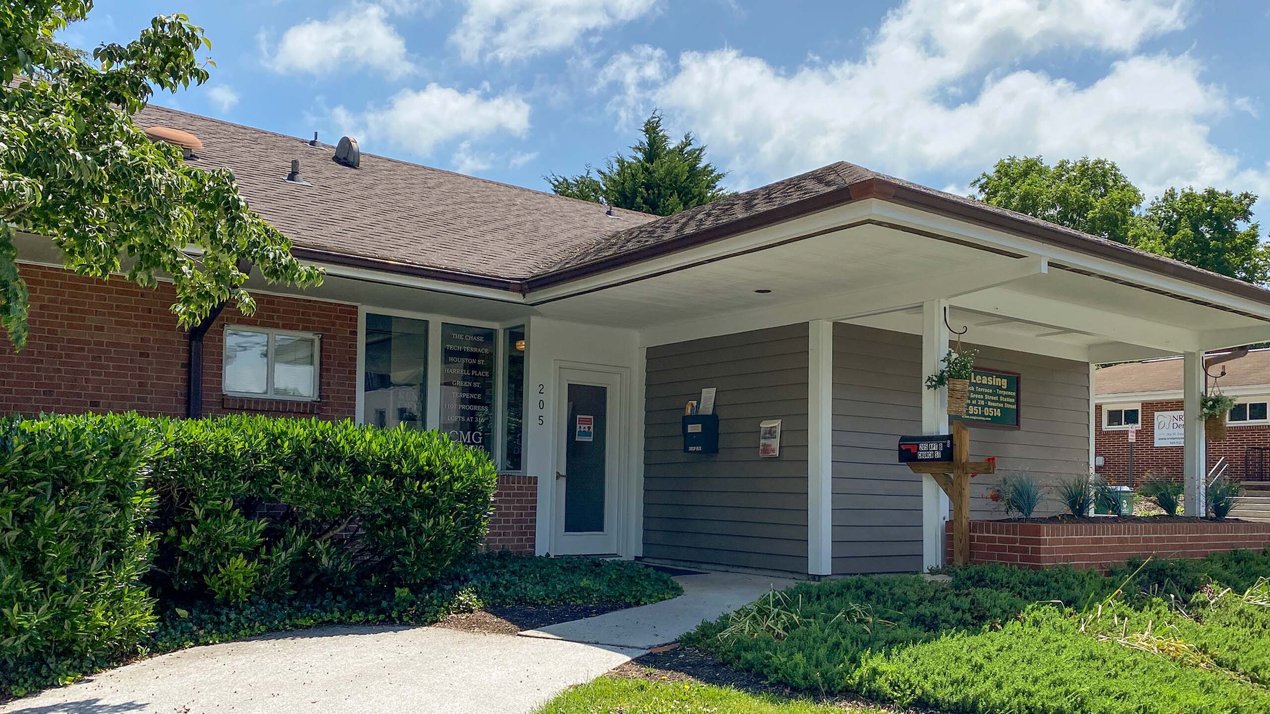 Charming leasing office exterior showcasing well-maintained landscaping and inviting entryway under a bright blue sky.