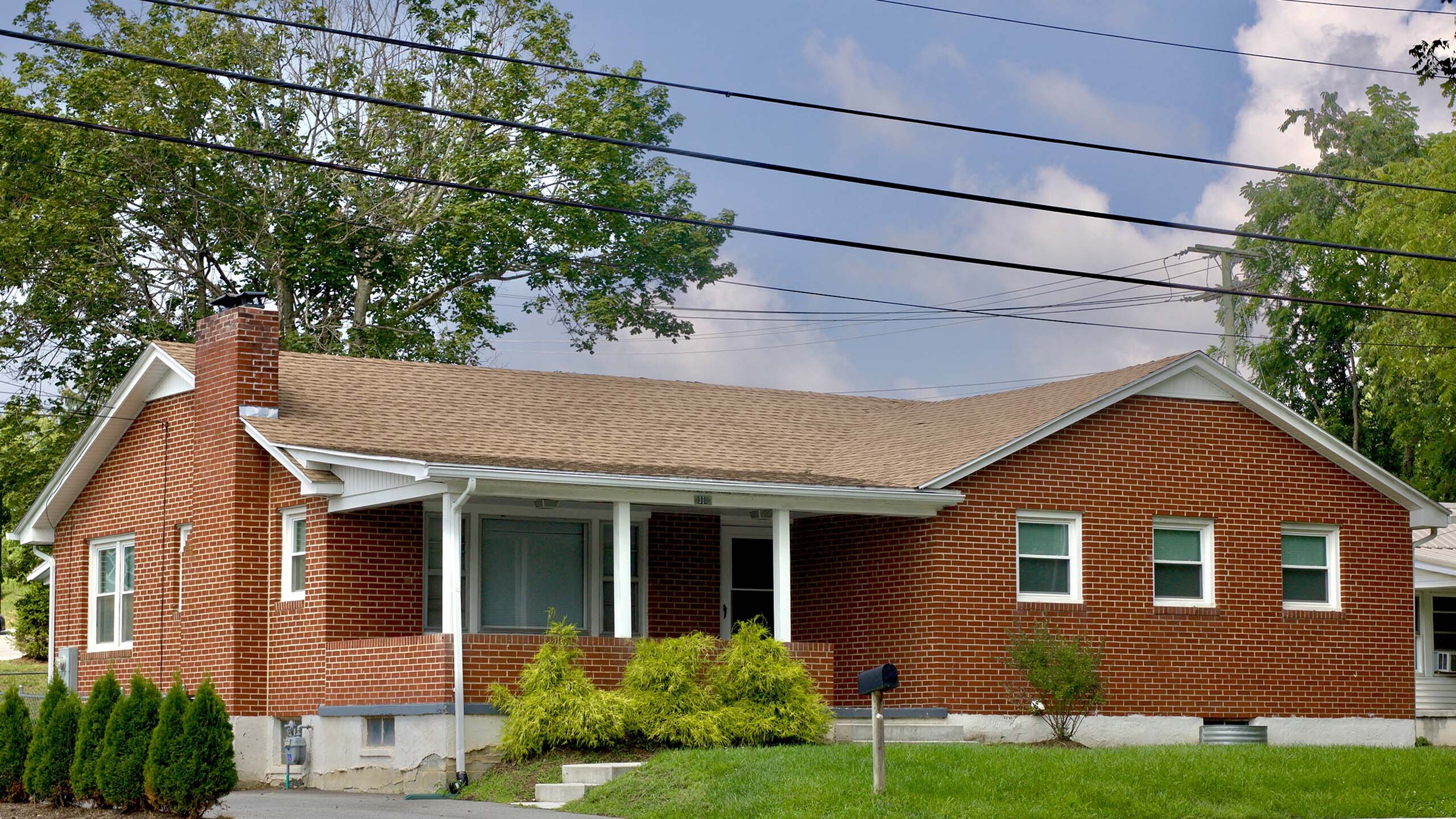 Charming brick home with a spacious front yard, nestled in a serene neighborhood with lush greenery.