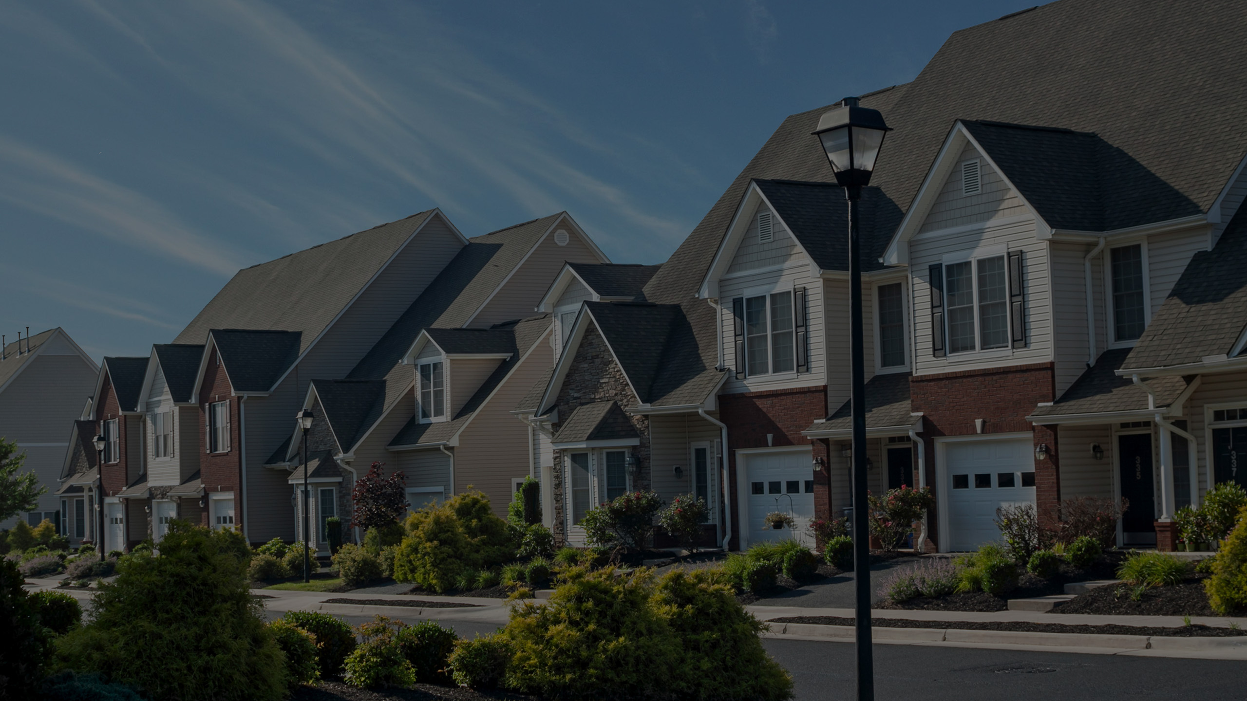 Charming residential street with elegant, multi-story homes featuring well-maintained gardens and inviting front porches.