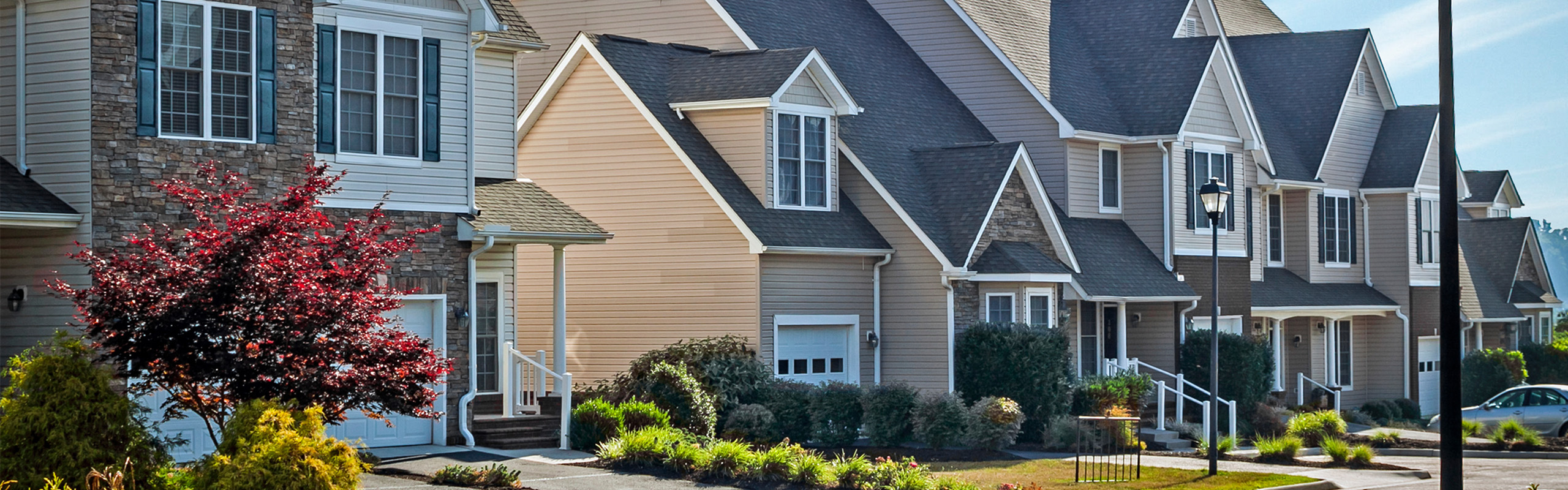 Charming residential street featuring elegant townhouses with stone accents, lush landscaping, and welcoming front porches.