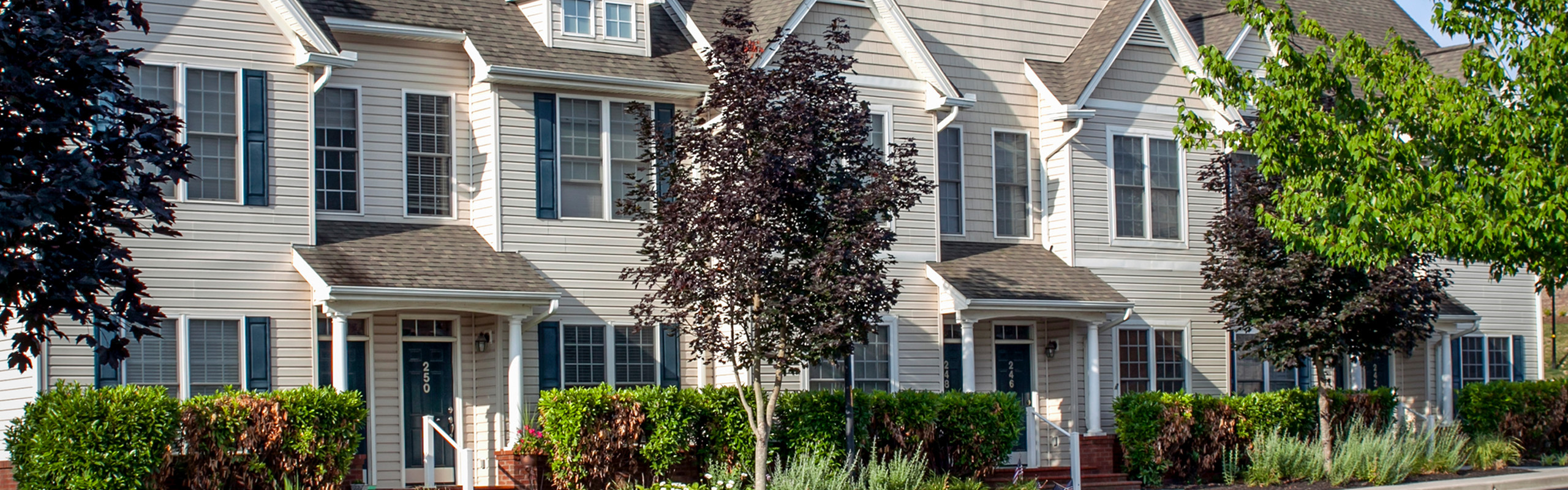 Charming row of modern townhouses with elegant facades, lush landscaping, and inviting entrances, perfect for family living.