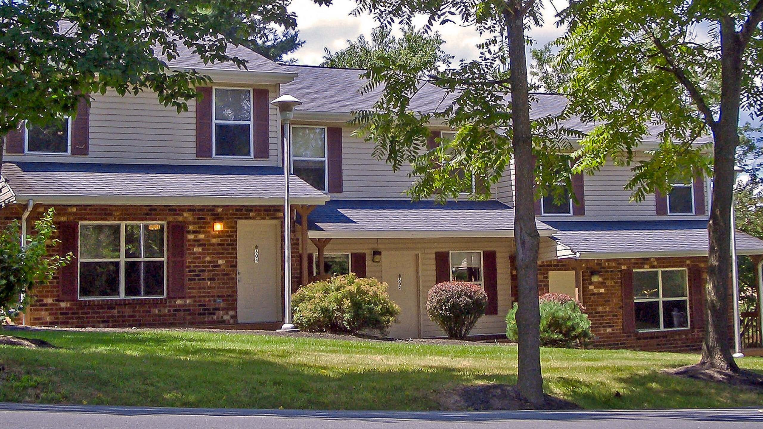 Charming townhome exterior featuring brick facade, lush greenery, and a cozy front porch.