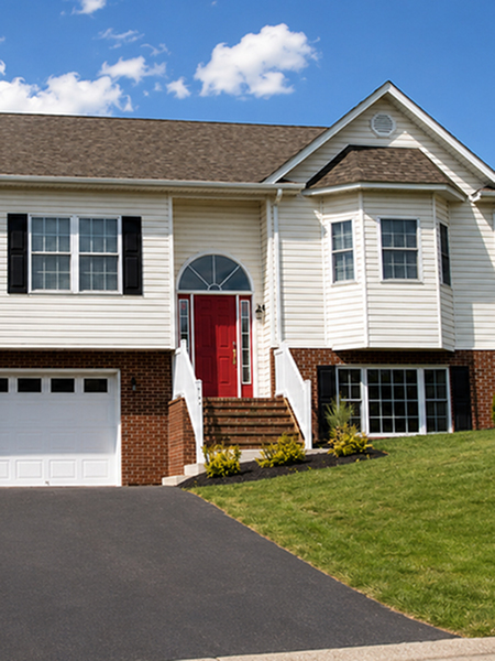 Charming suburban home with a vibrant red door, well-maintained lawn, and a spacious driveway under a bright blue sky.