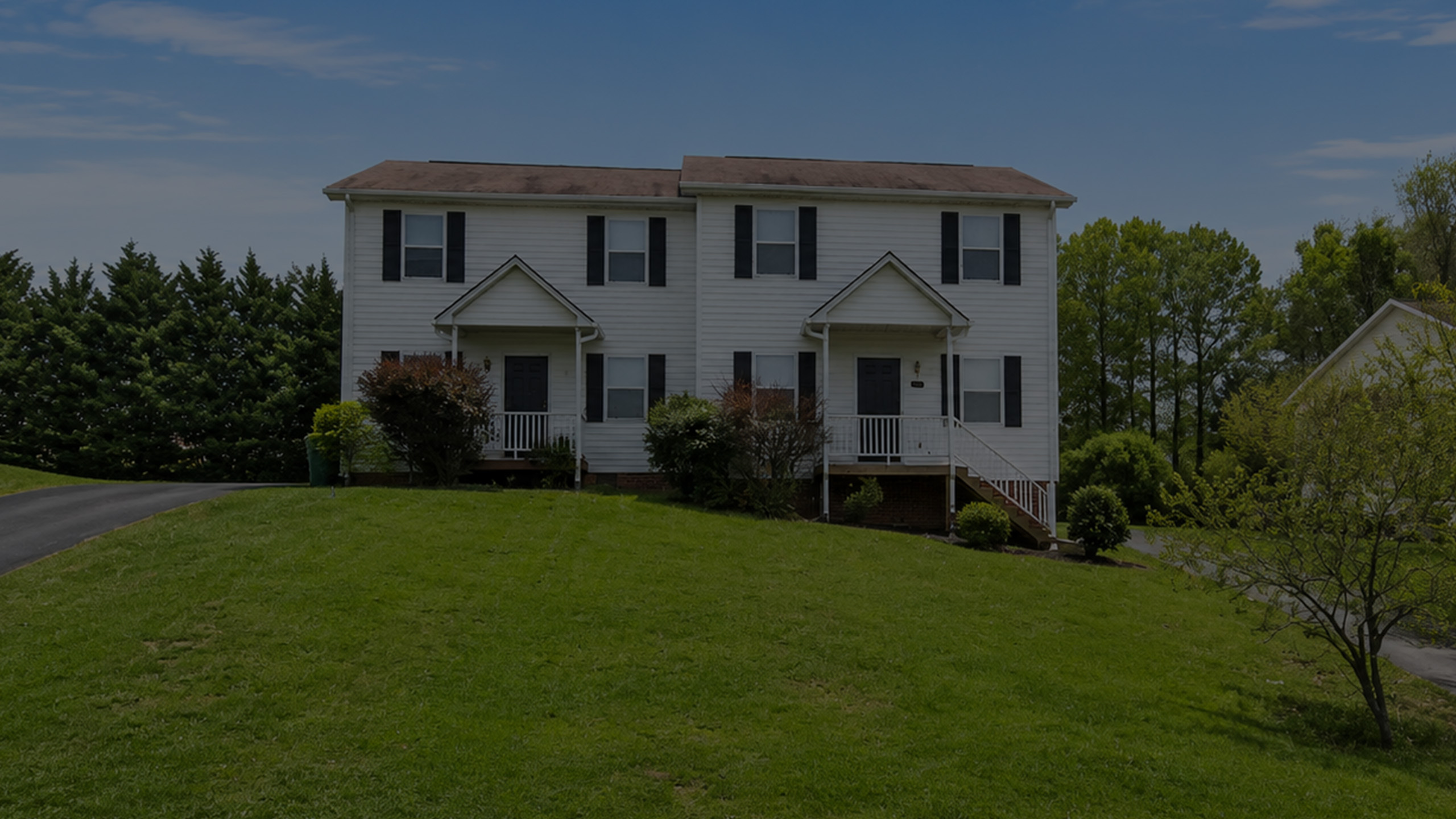 Charming duplex home with classic white facade and inviting front porches, set on a lush green lawn.