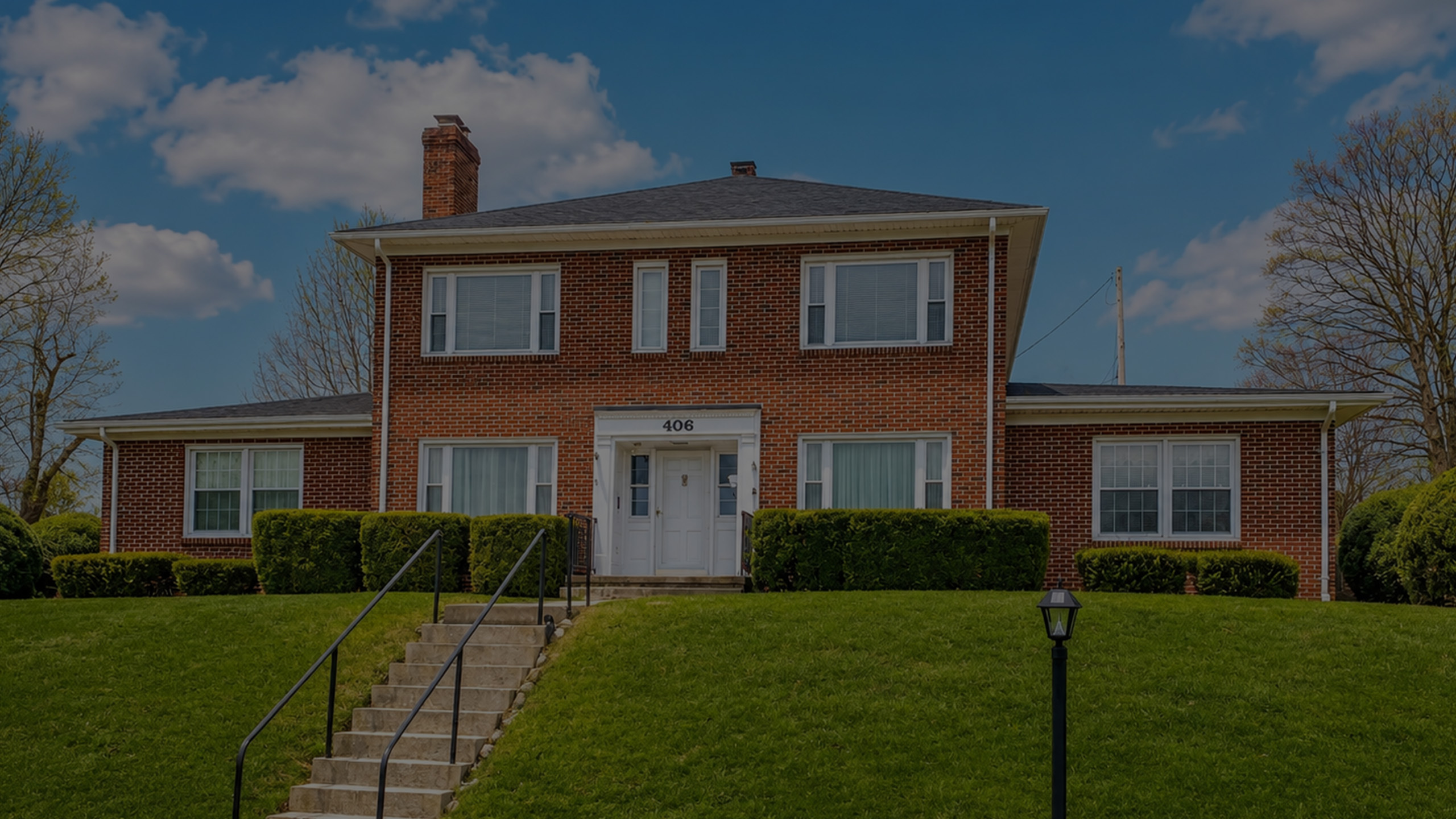 Charming two-story brick home with elegant windows, surrounded by lush greenery and a welcoming front entrance.