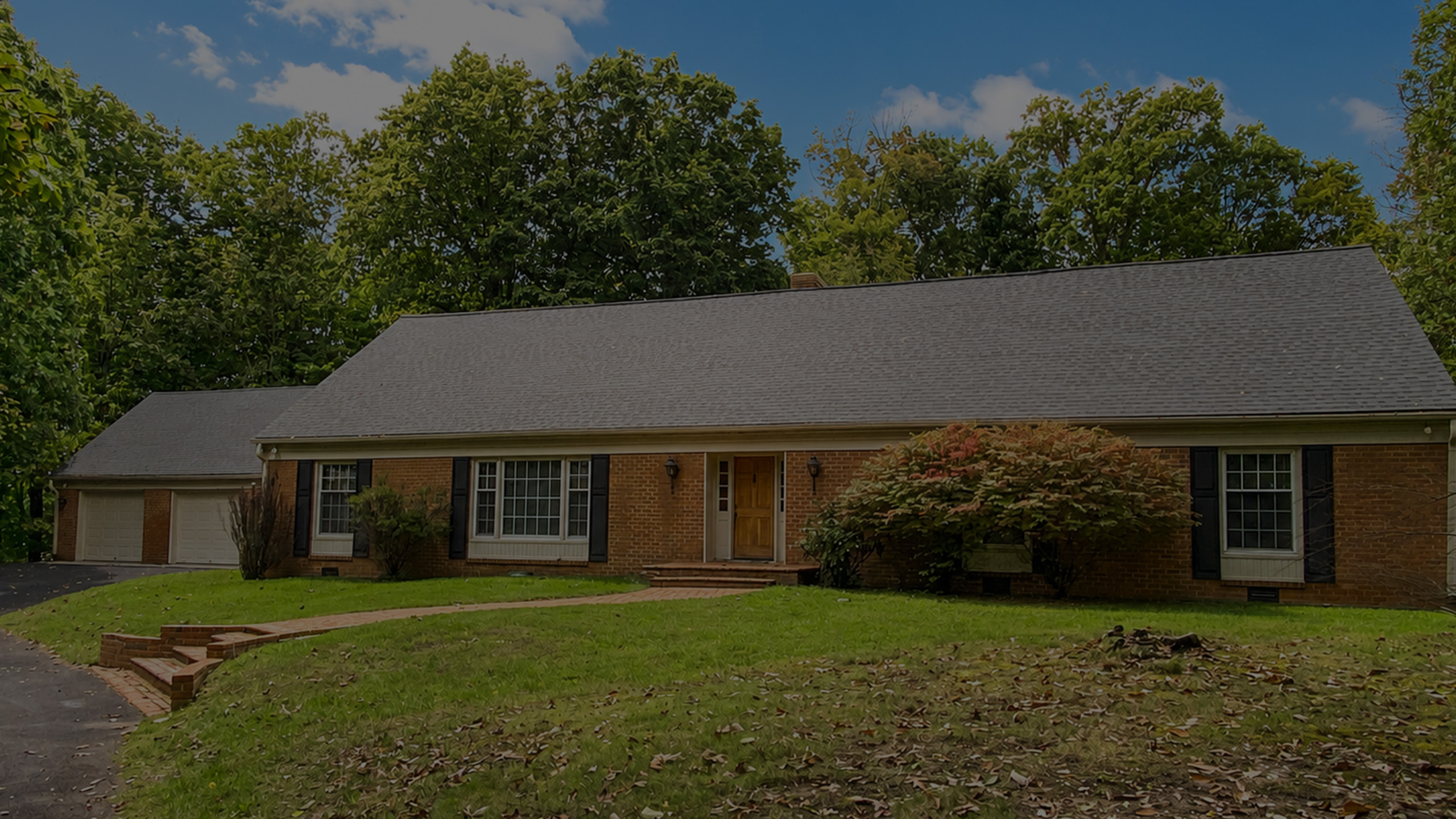 Charming brick ranch-style home with spacious front lawn, surrounded by lush trees, featuring a double garage and inviting entrance.