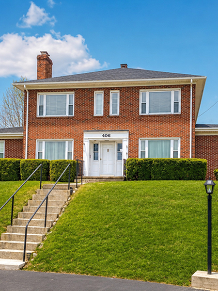 Charming two-story brick residence with large windows, lush green lawn, and welcoming entrance.