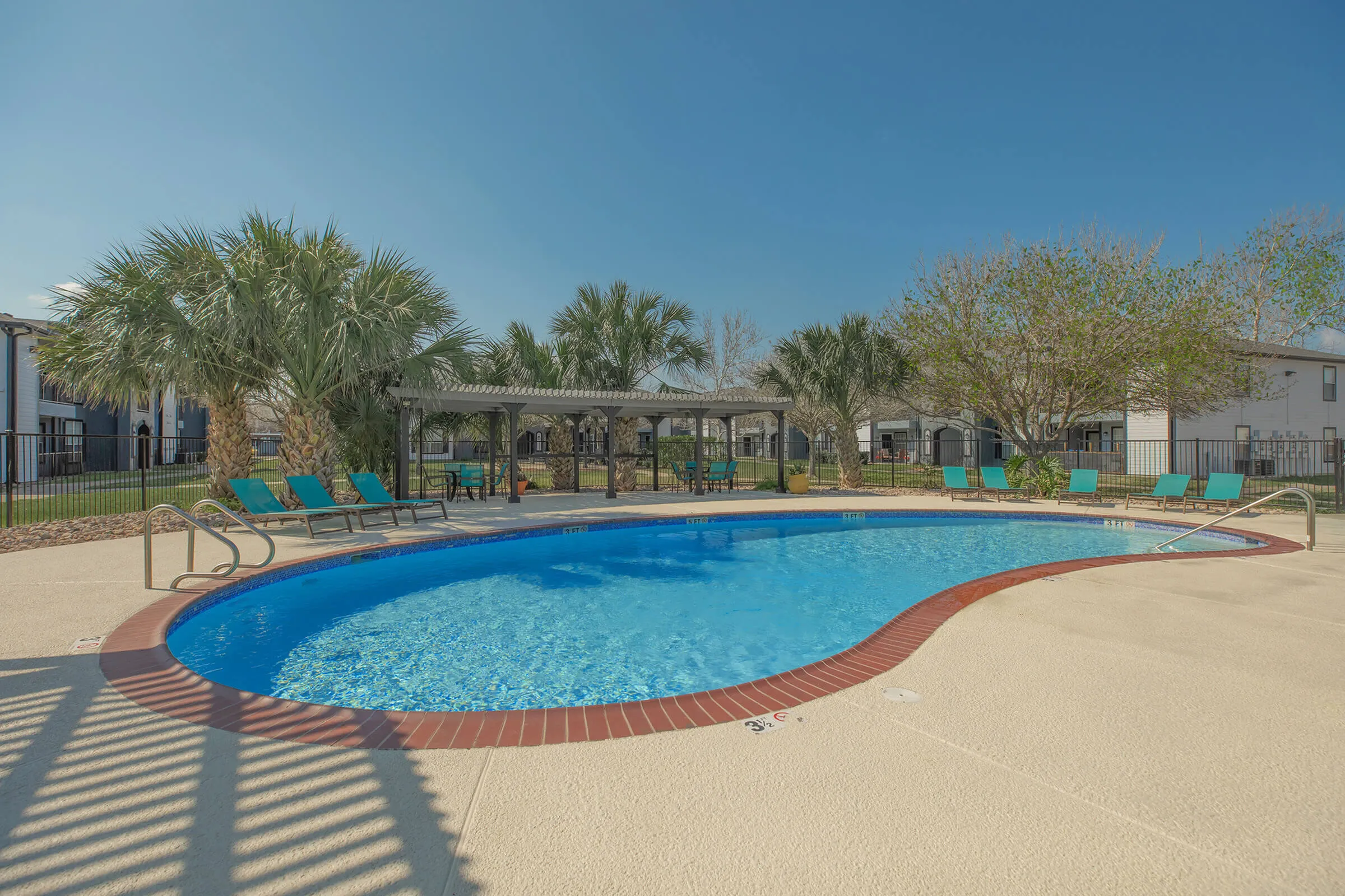 Inviting outdoor pool area with modern lounge chairs, surrounded by lush palm trees and a pergola, perfect for relaxation.
