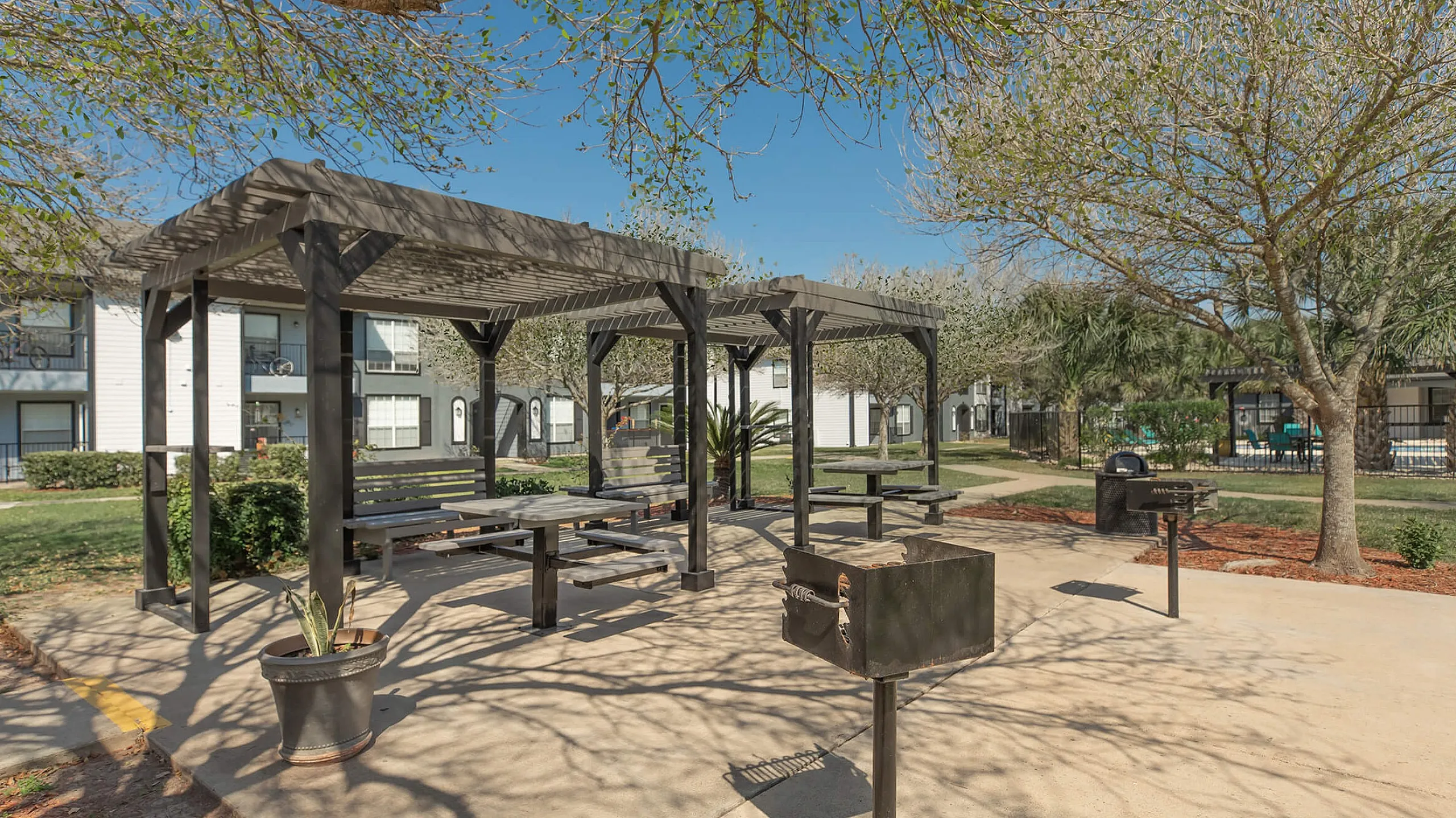Inviting outdoor seating area with a stylish pergola, surrounded by lush greenery and modern apartment buildings.