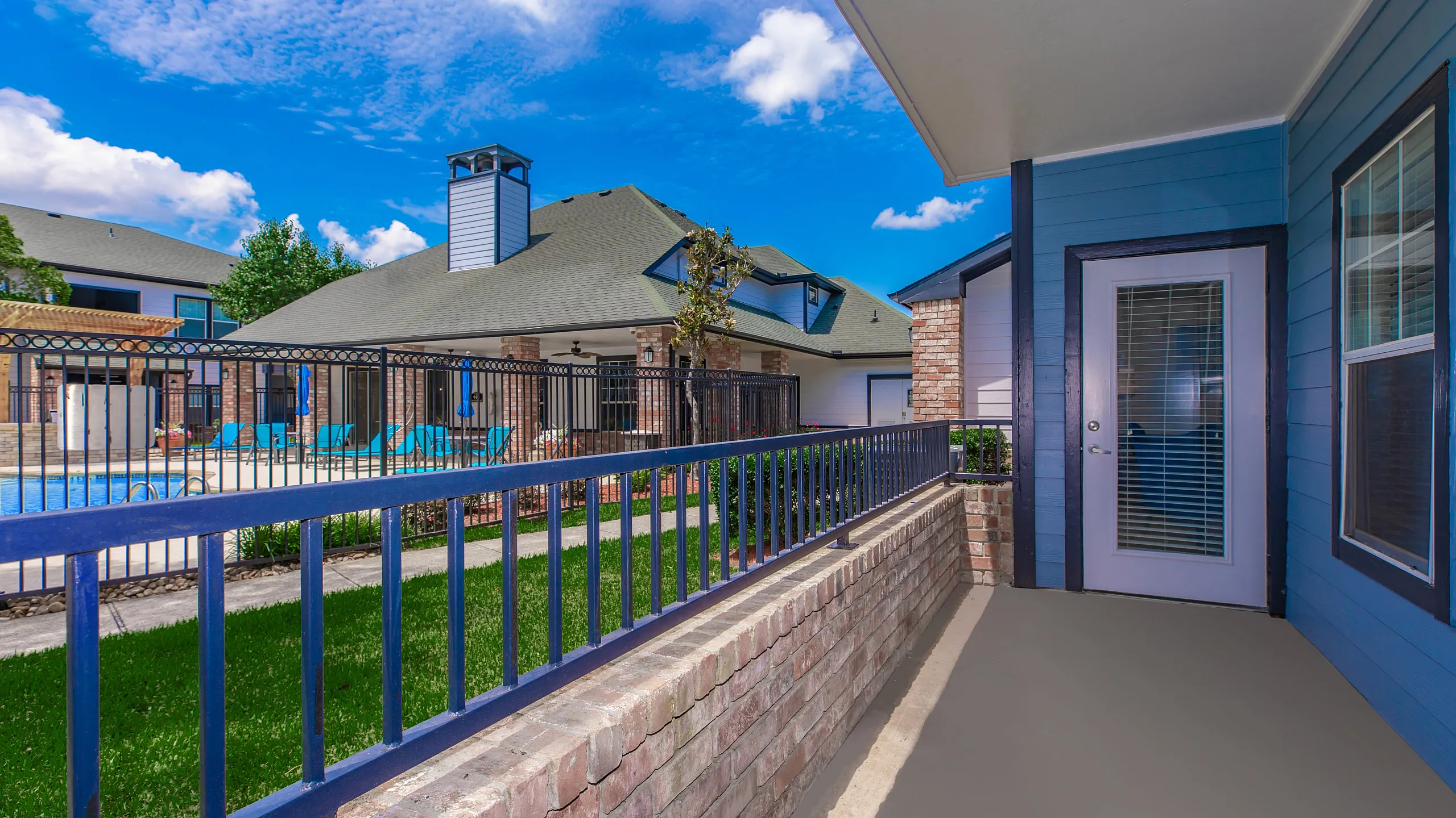 Inviting apartment patio overlooking a vibrant pool area, ideal for relaxation and entertaining in a sunny outdoor setting.