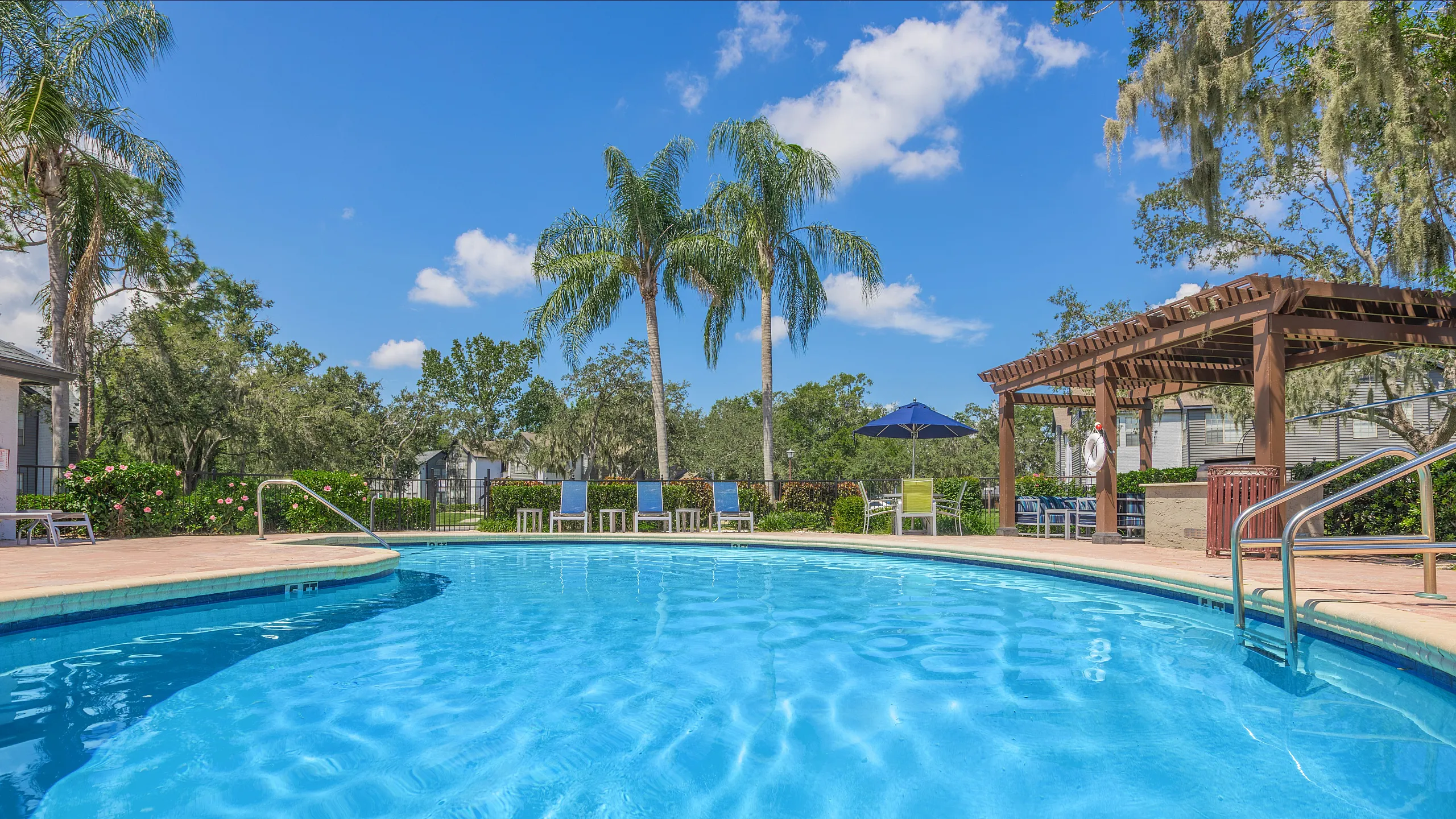 Inviting outdoor pool area surrounded by lush greenery, palm trees, and a stylish pergola, perfect for relaxation and enjoyment.