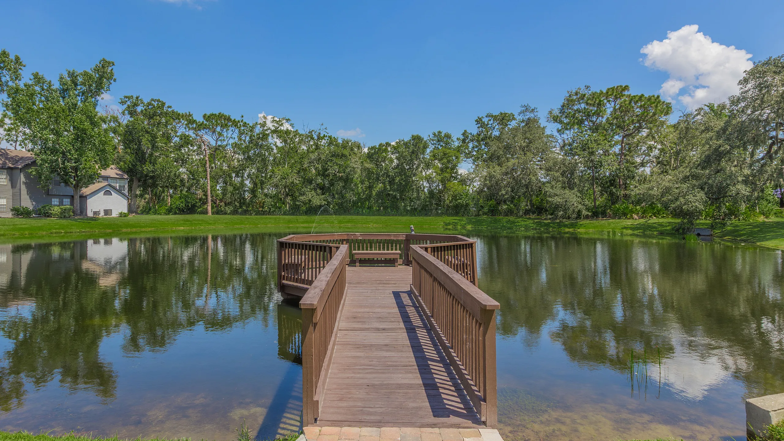 Tranquil lakeside view with a charming wooden dock surrounded by lush greenery and blue skies.