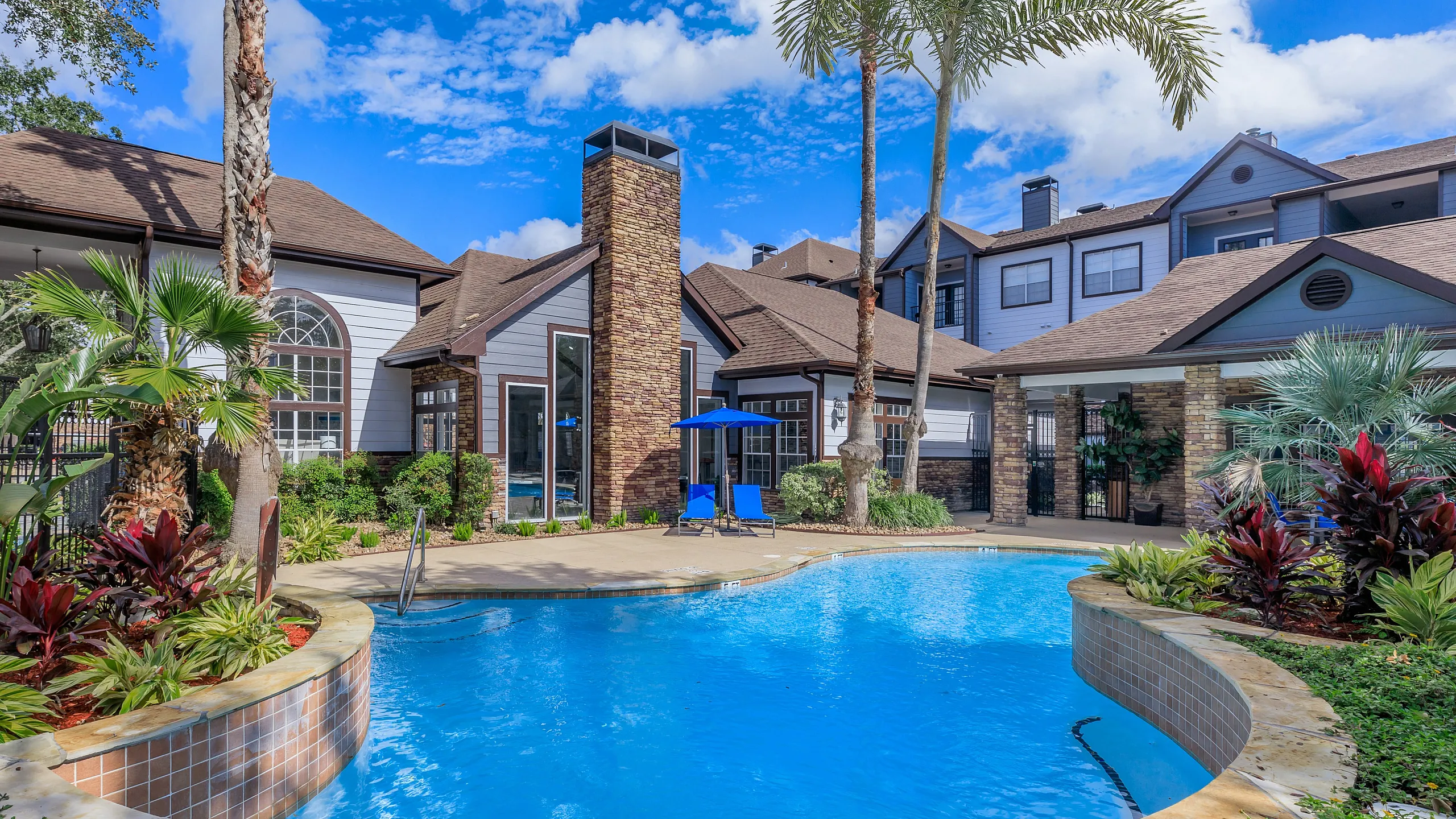 Luxurious apartment complex with a sparkling pool surrounded by lush greenery and elegant architecture, perfect for relaxation and enjoyment.