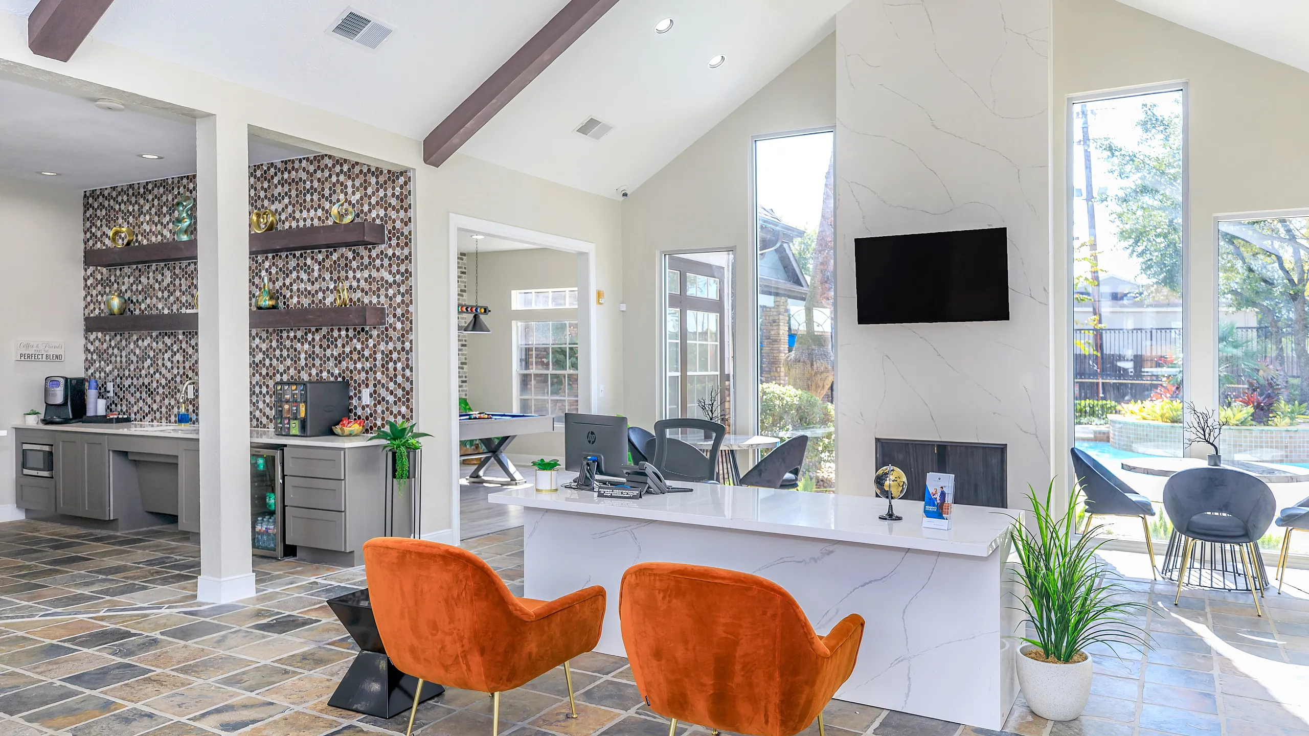 Bright and modern office space with high ceilings, stylish orange chairs, and a sleek reception desk, overlooking a sunny garden area.