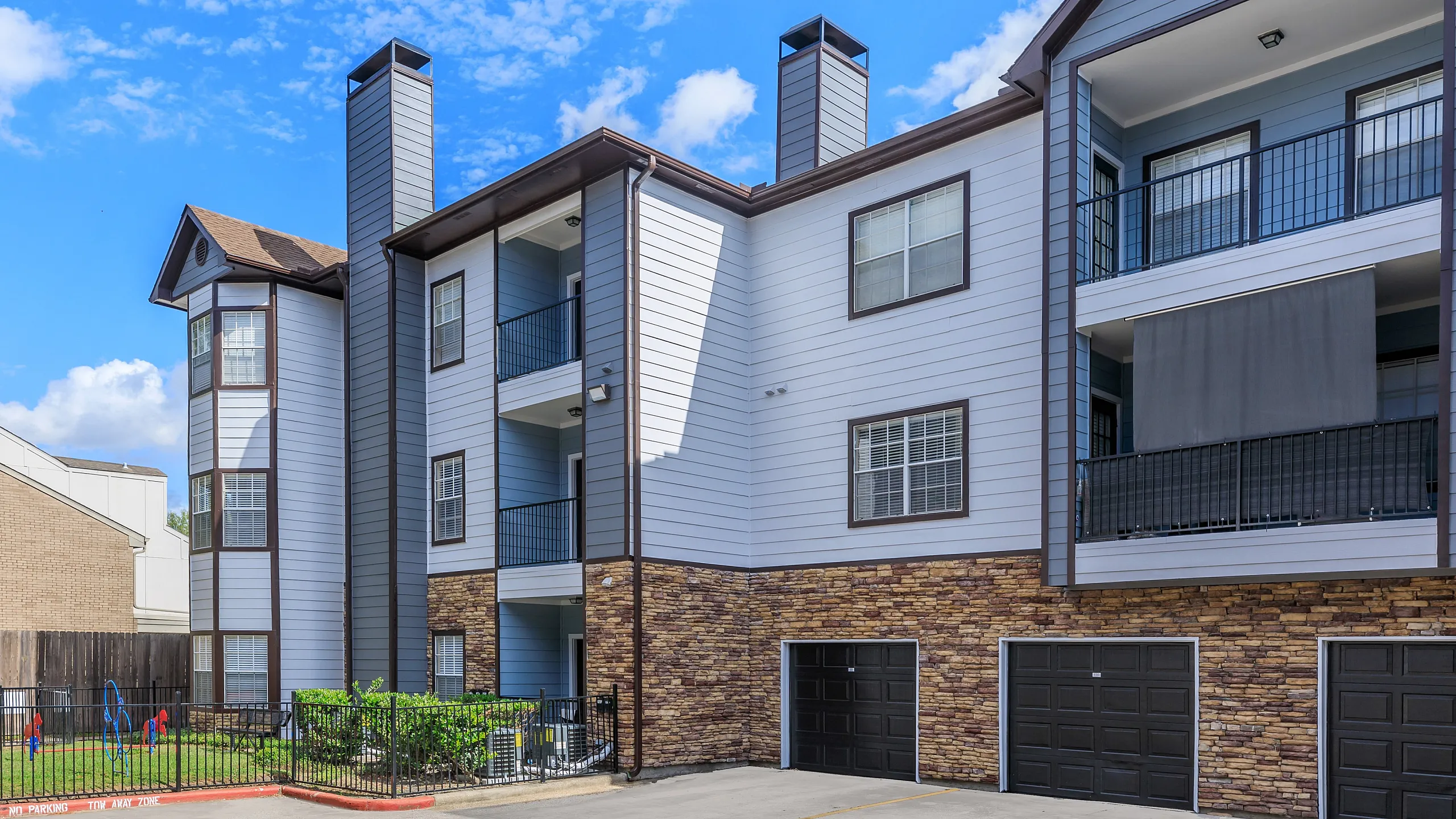 Charming modern apartment building with unique stone accents, spacious balconies, and a leisure playground surrounded by lush greenery.