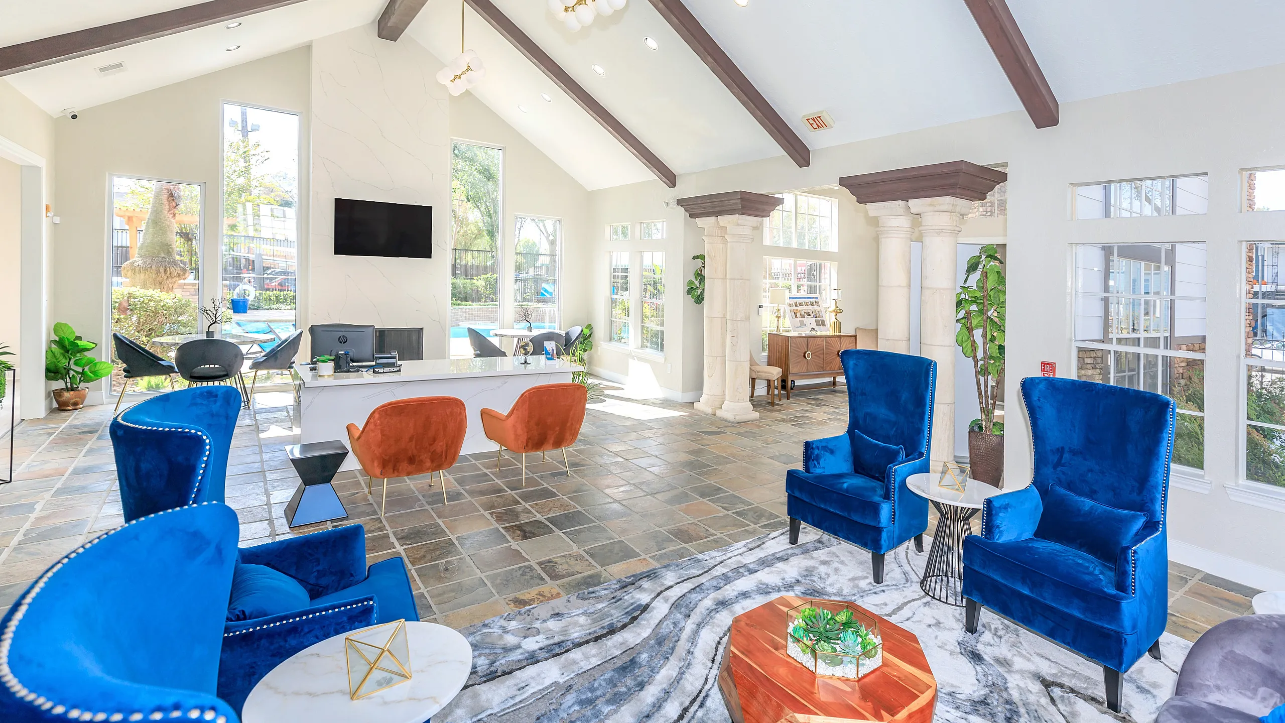 Elegant and spacious apartment lounge featuring plush blue and orange seating, stylish decor, and abundant natural light.