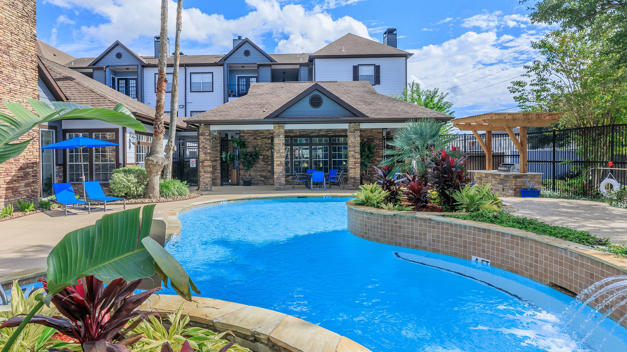 Charming apartment complex with a sparkling pool, lush landscaping, and inviting outdoor seating.