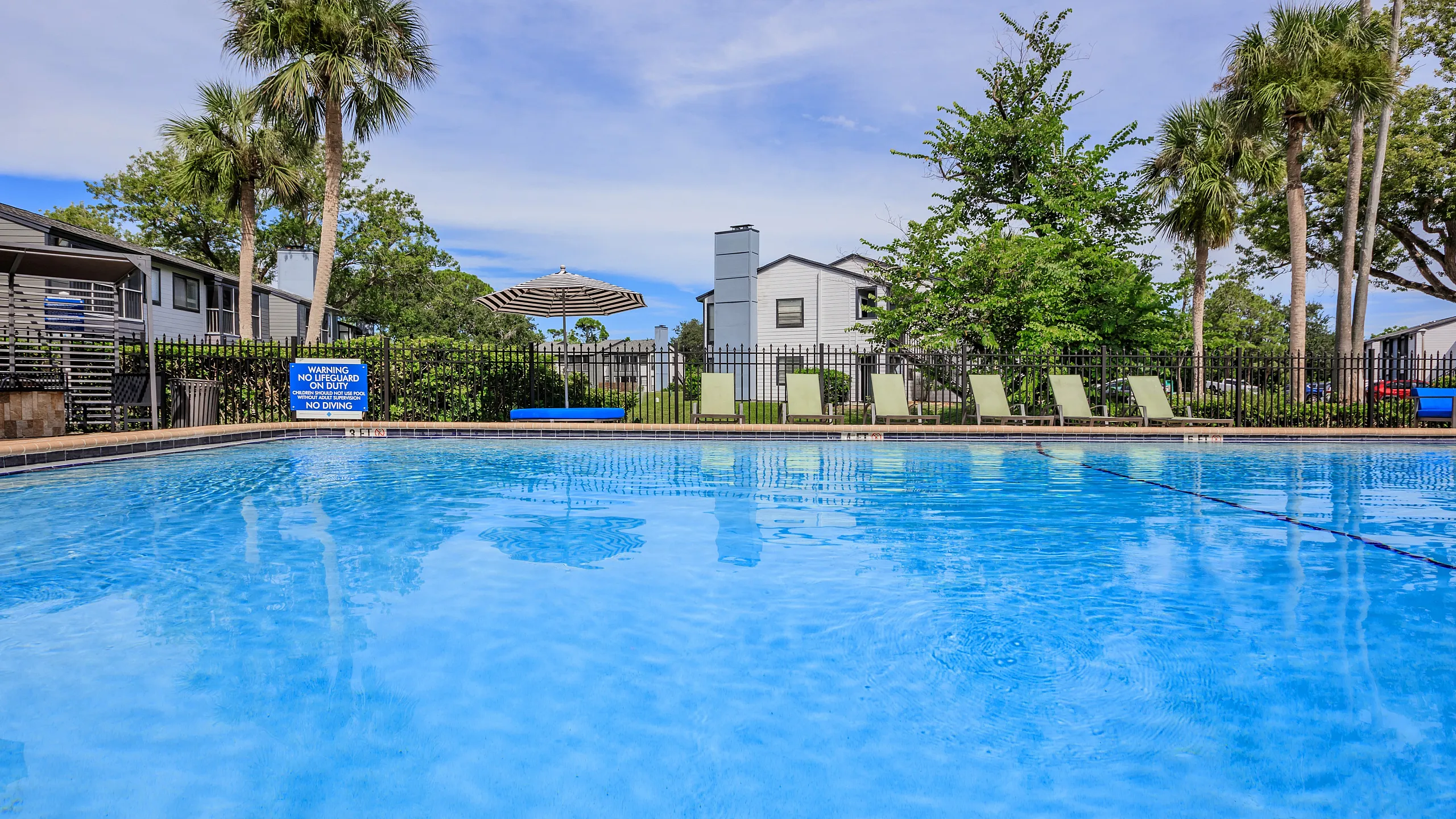 Inviting outdoor pool area with clear blue water, surrounded by lush greenery and comfortable lounge chairs, perfect for relaxation.