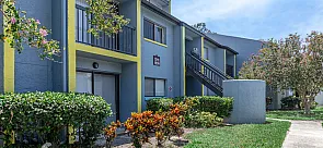 Charming apartment exterior with vibrant landscaping, featuring a modern blue facade with yellow accents and private balconies.