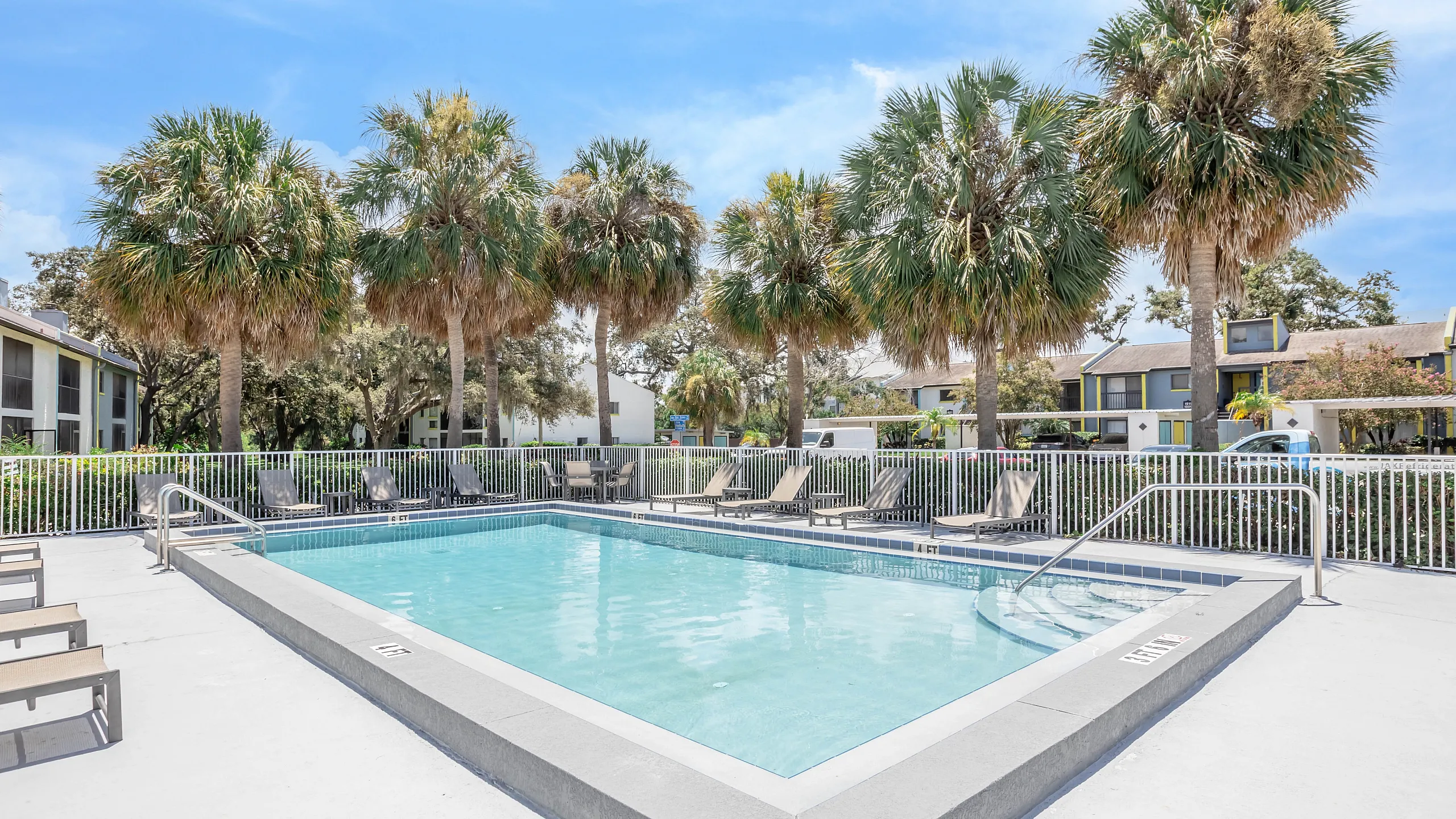 Inviting outdoor pool area surrounded by lush palm trees and modern lounge chairs, offering a serene retreat in a vibrant apartment community.