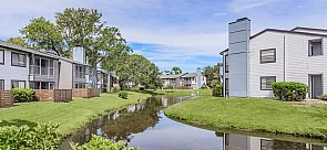 Charming apartment complex with serene water views and lush greenery, offering peaceful living in a nature-inspired setting.