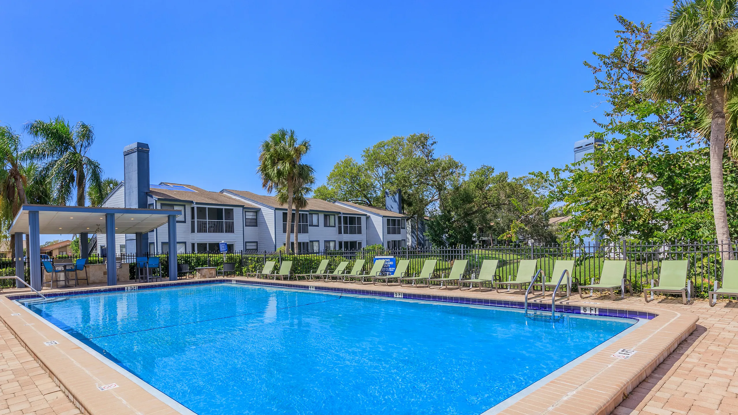 Inviting apartment complex with a sparkling outdoor pool surrounded by lush greenery and comfortable lounge chairs.
