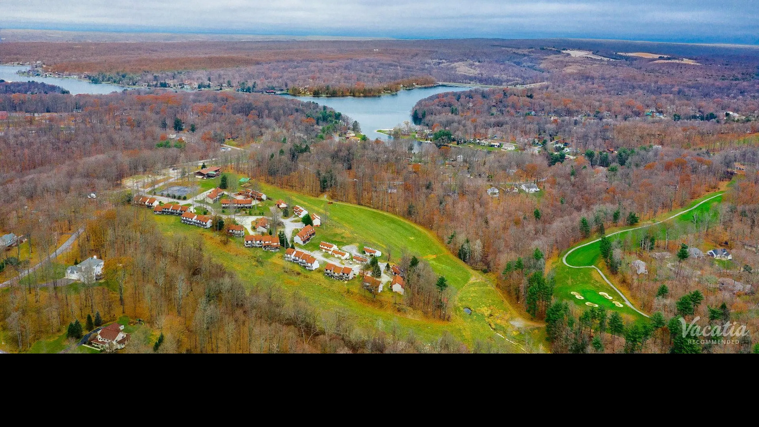 Breathtaking aerial view of a serene landscape with winding roads, charming cottages, and a tranquil lake surrounded by lush forests.
