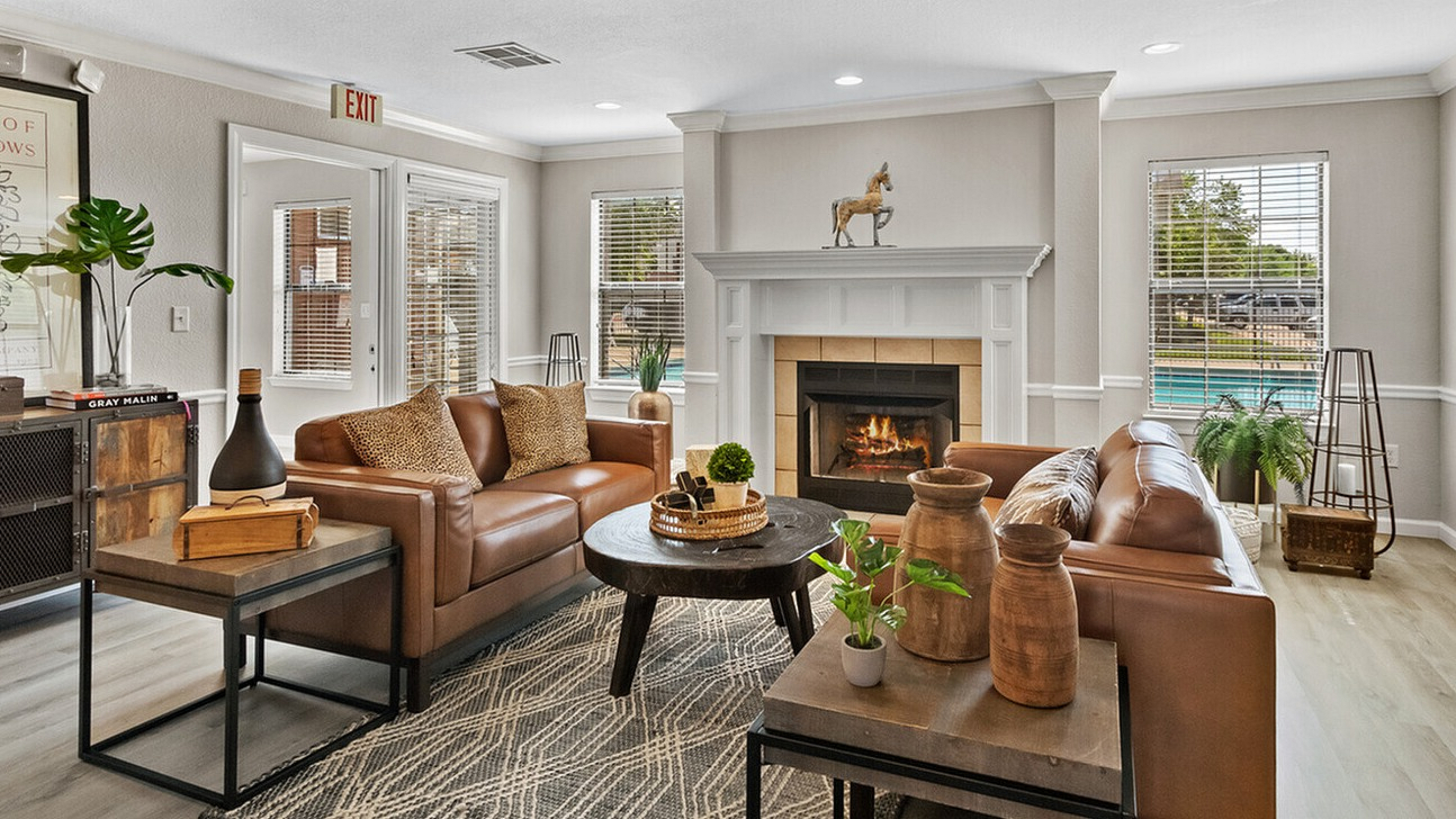 Elegant living room with cozy leather sofas, a chic fireplace, and large windows offering a pool view, perfect for relaxation and style.